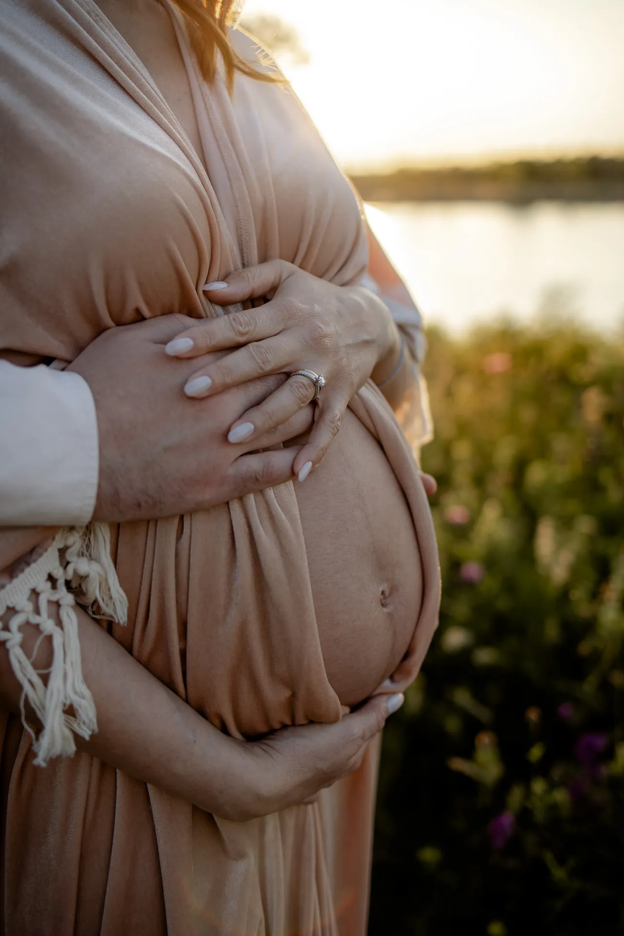 Pregnant woman holds baby bump in golden sunset by the water