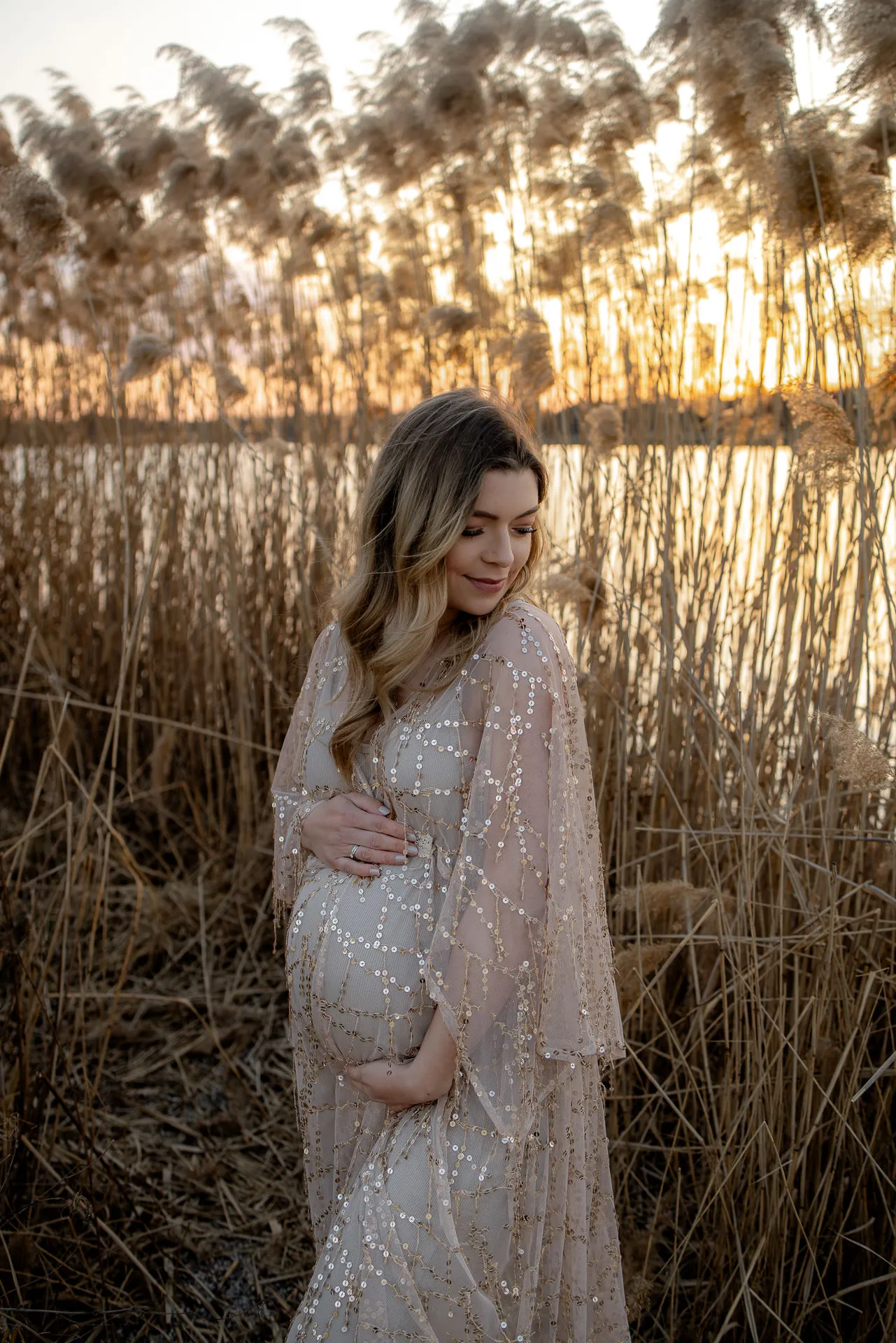 Pregnant woman in sparkling dress at sunset in reed grass field
