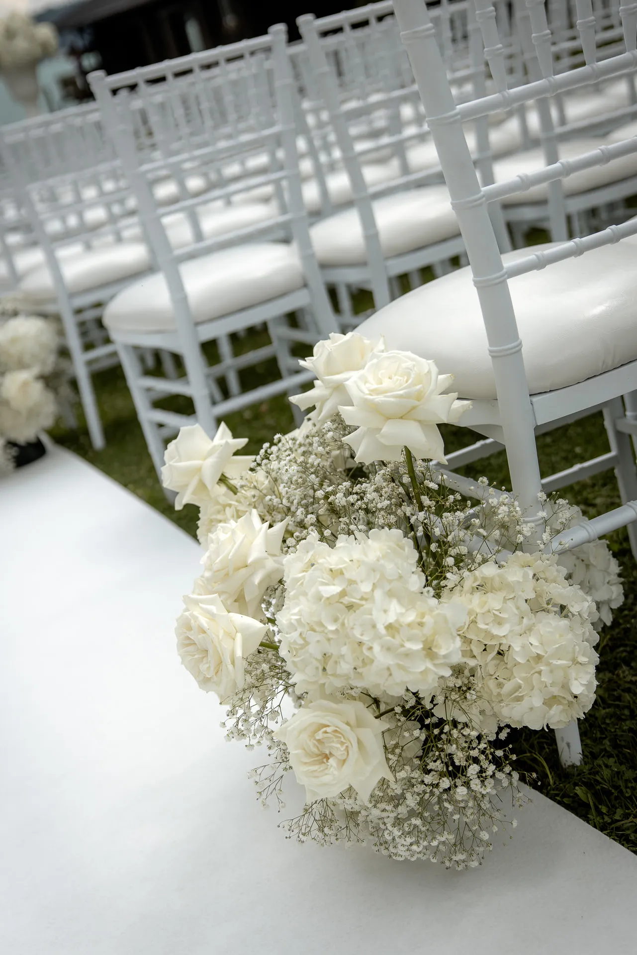 Elegant flower bouquet on white Chiavari chairs at garden wedding ceremony