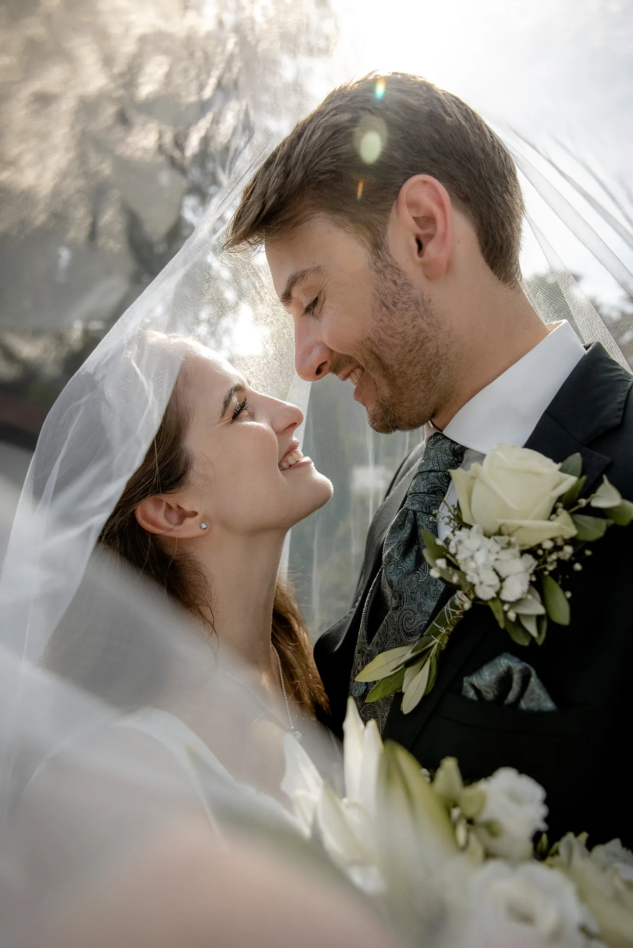 Wedding couple Miriam and Benedikt in intimate embrace under bridal veil with backlight at authentic country wedding