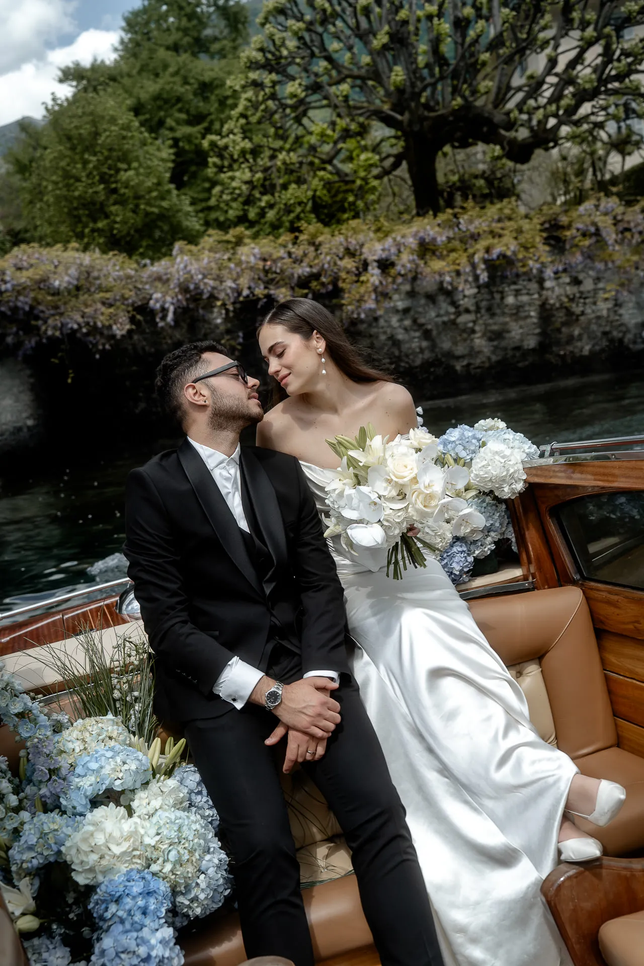 Wedding couple in Venetian motorboat under wisteria pergola at Lake Como