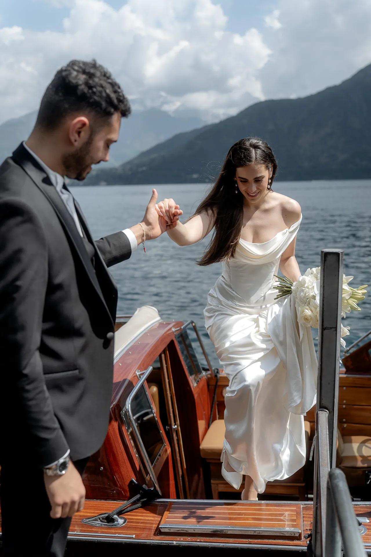 Groom helping bride exit luxury motorboat at Lake Como