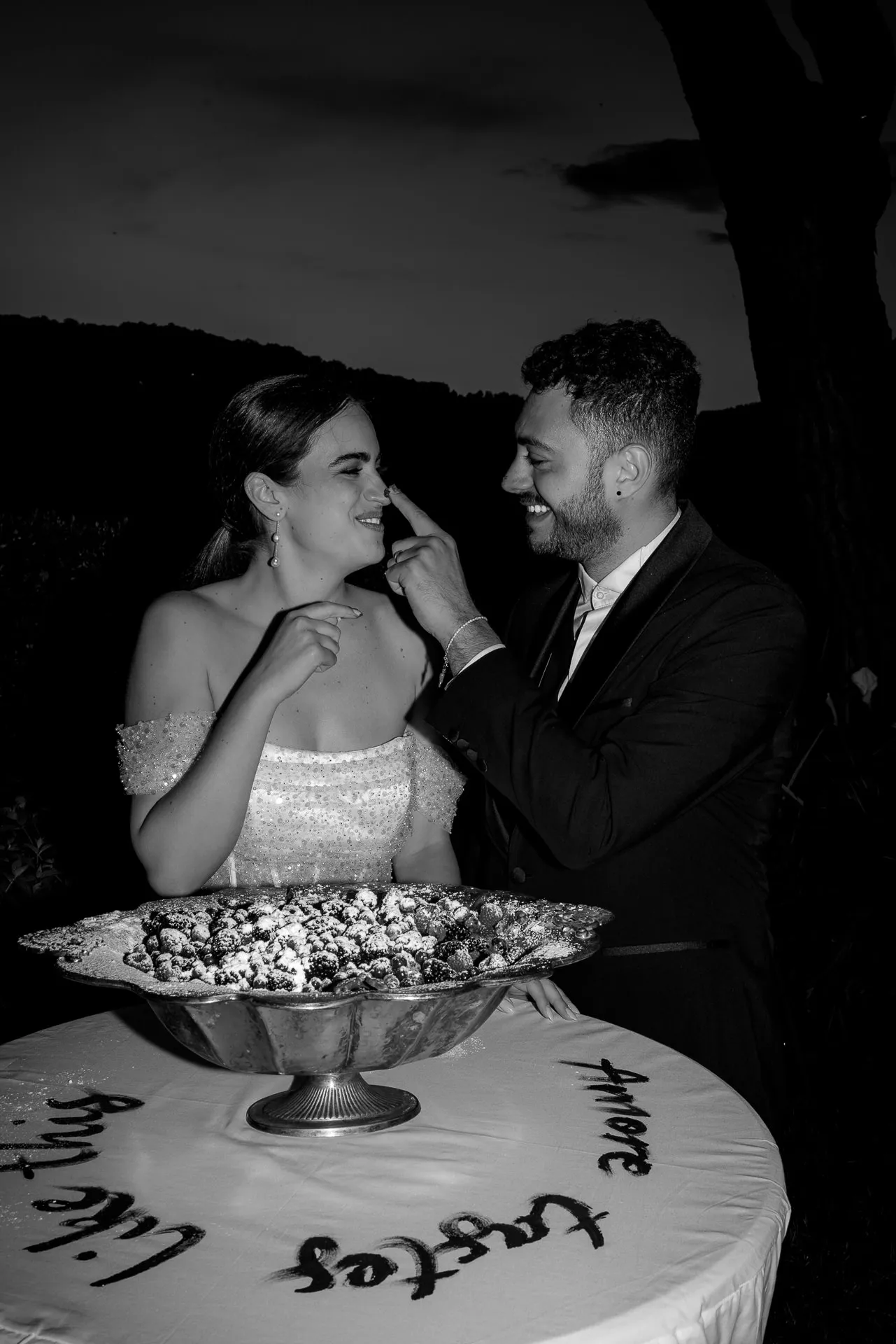 Wedding couple feeding each other at nighttime reception Villa Balbiano black and white
