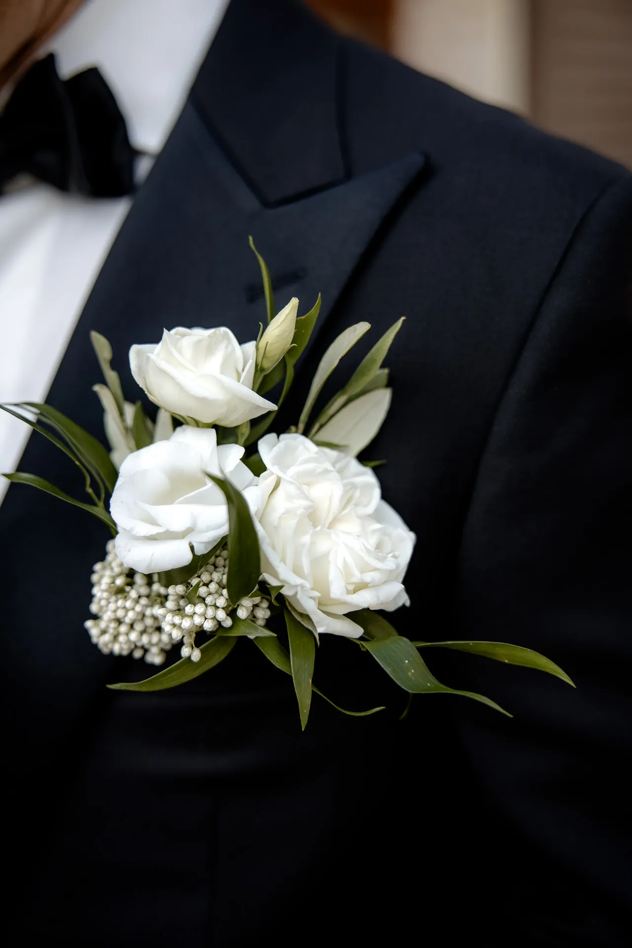 Groom's boutonniere with white roses and baby's breath on black tuxedo
