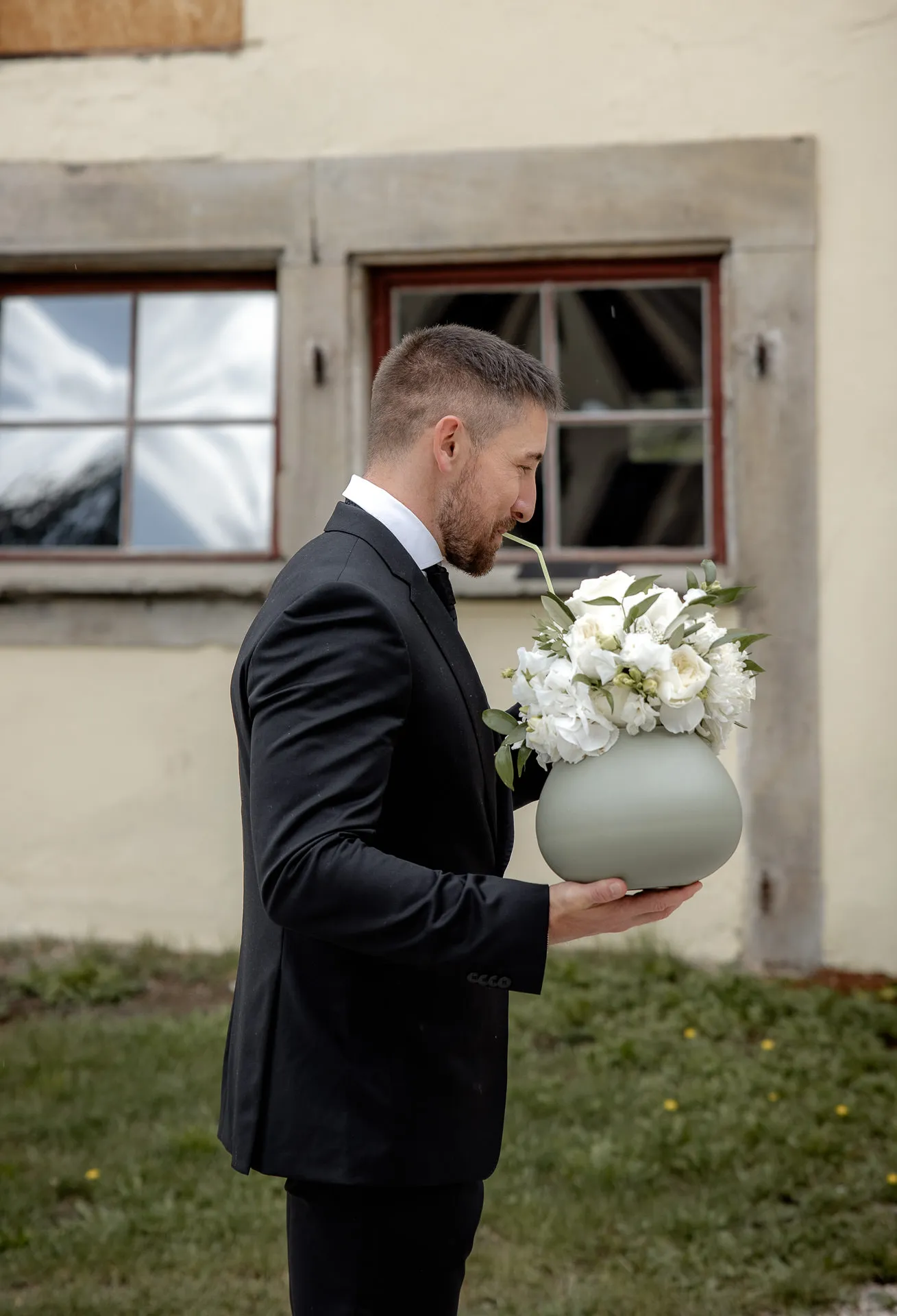 Groom with white bridal bouquet in green vase in front of Schloss Eyrichshof