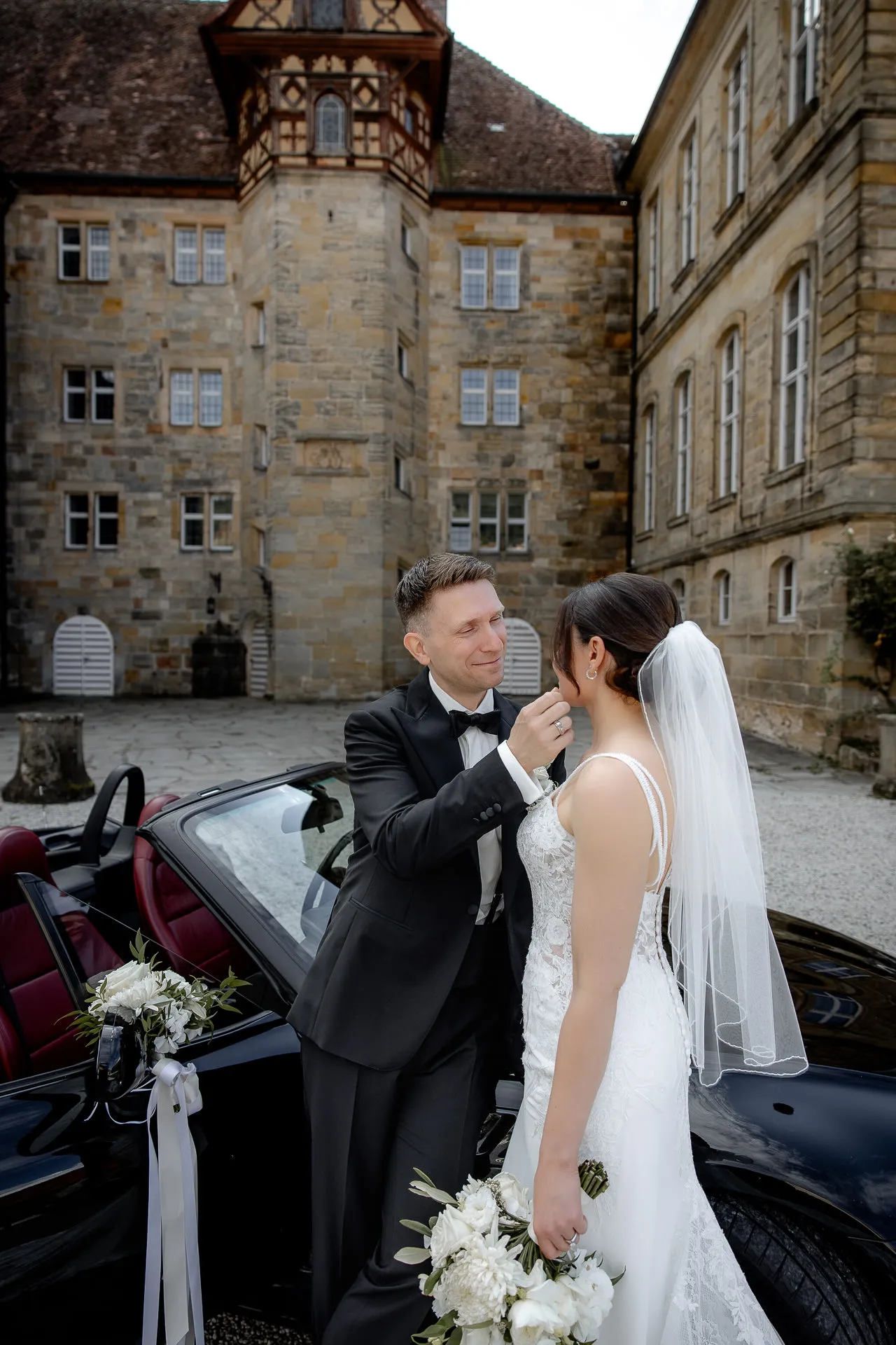 Tender moment between bride and groom at convertible in front of Schloss Eyrichshof