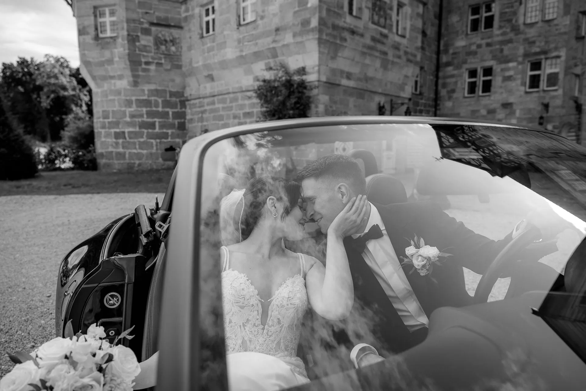 Intimate kiss in convertible car in front of Schloss Eyrichshof in black and white