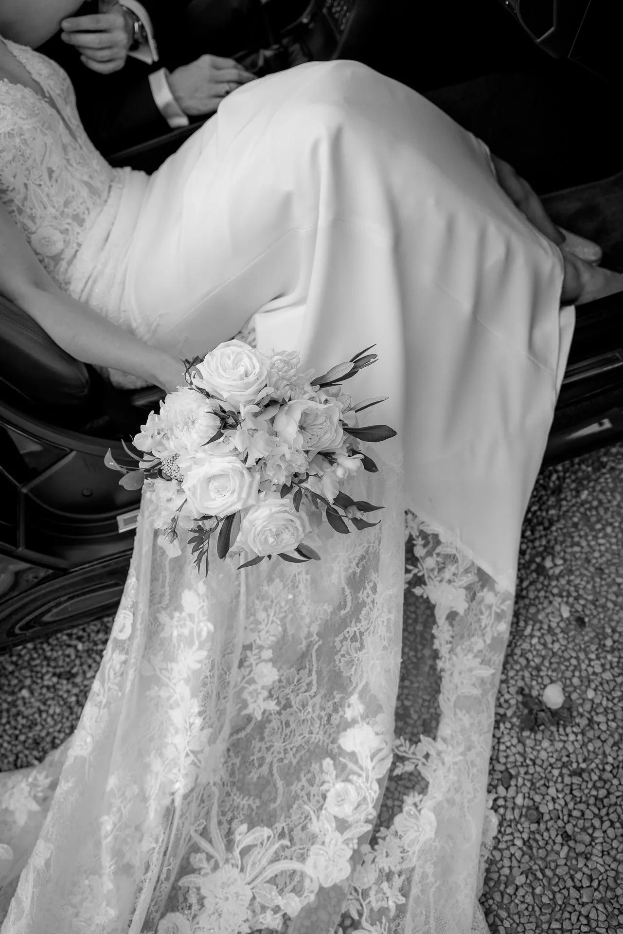 Bride in lace dress with bridal bouquet from convertible in black and white