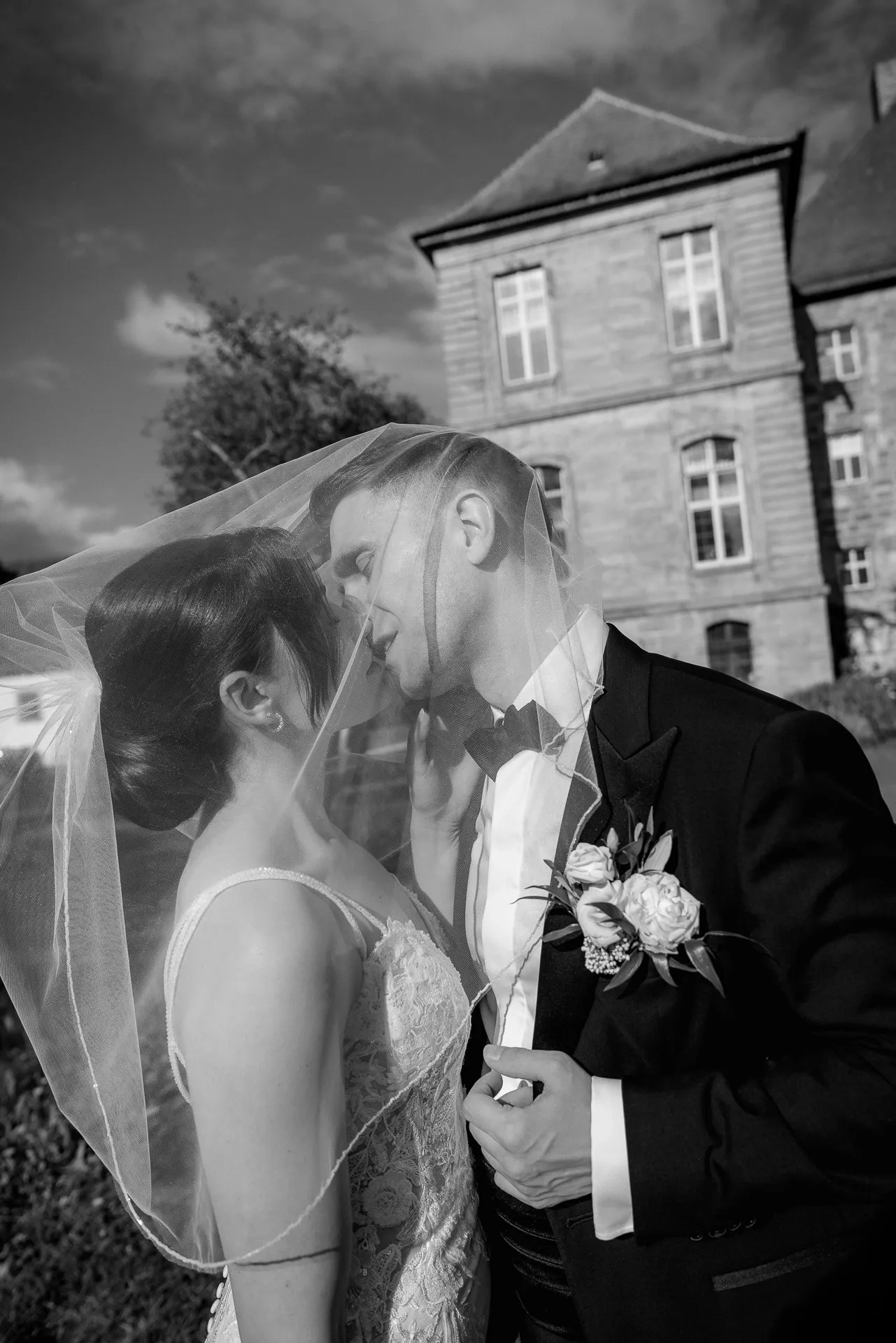 Romantic kiss under veil in front of Schloss Eyrichshof in black and white wedding photography