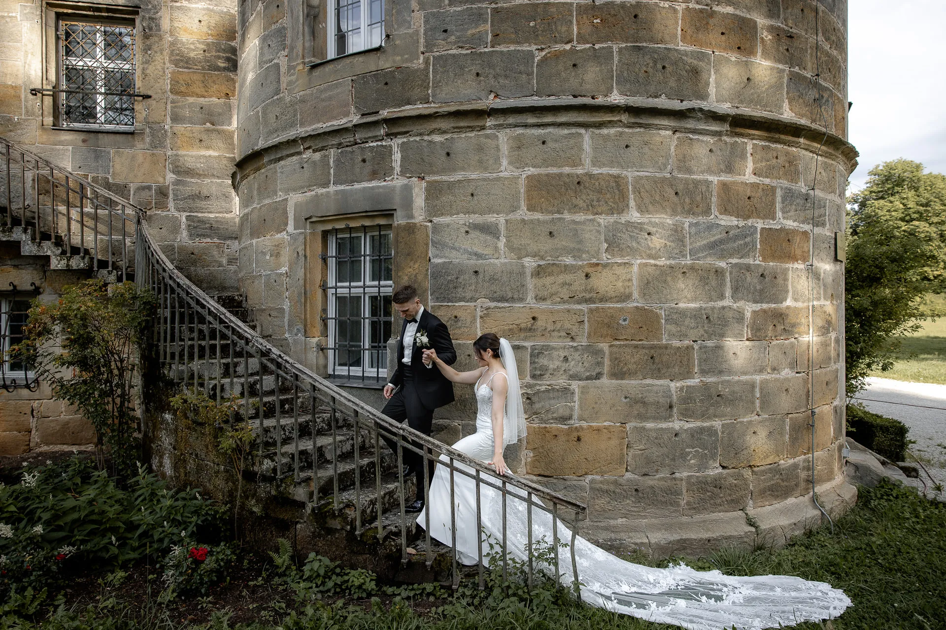 Bride and groom at historic Schloss Eyrichshof stairs with wedding dress and veil