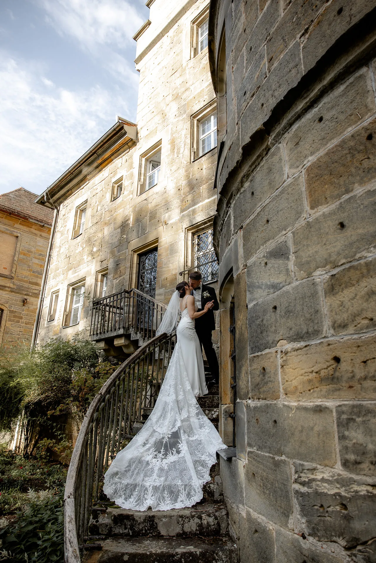 Romantic bride and groom at Schloss Eyrichshof stairs with lace veil and wedding dress