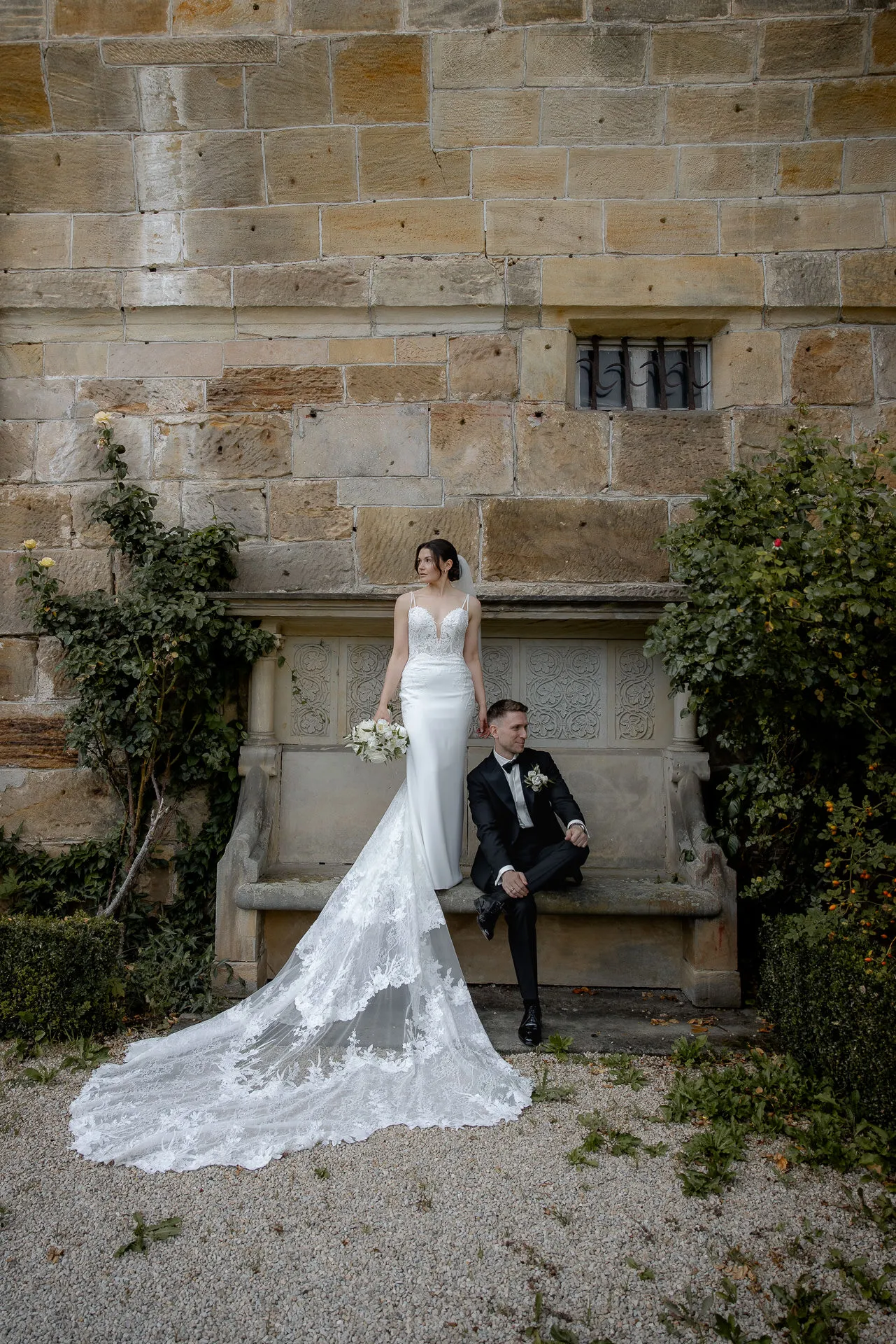 Elegant bride and groom at stone bench before historic castle wall Eyrichshof with lace veil