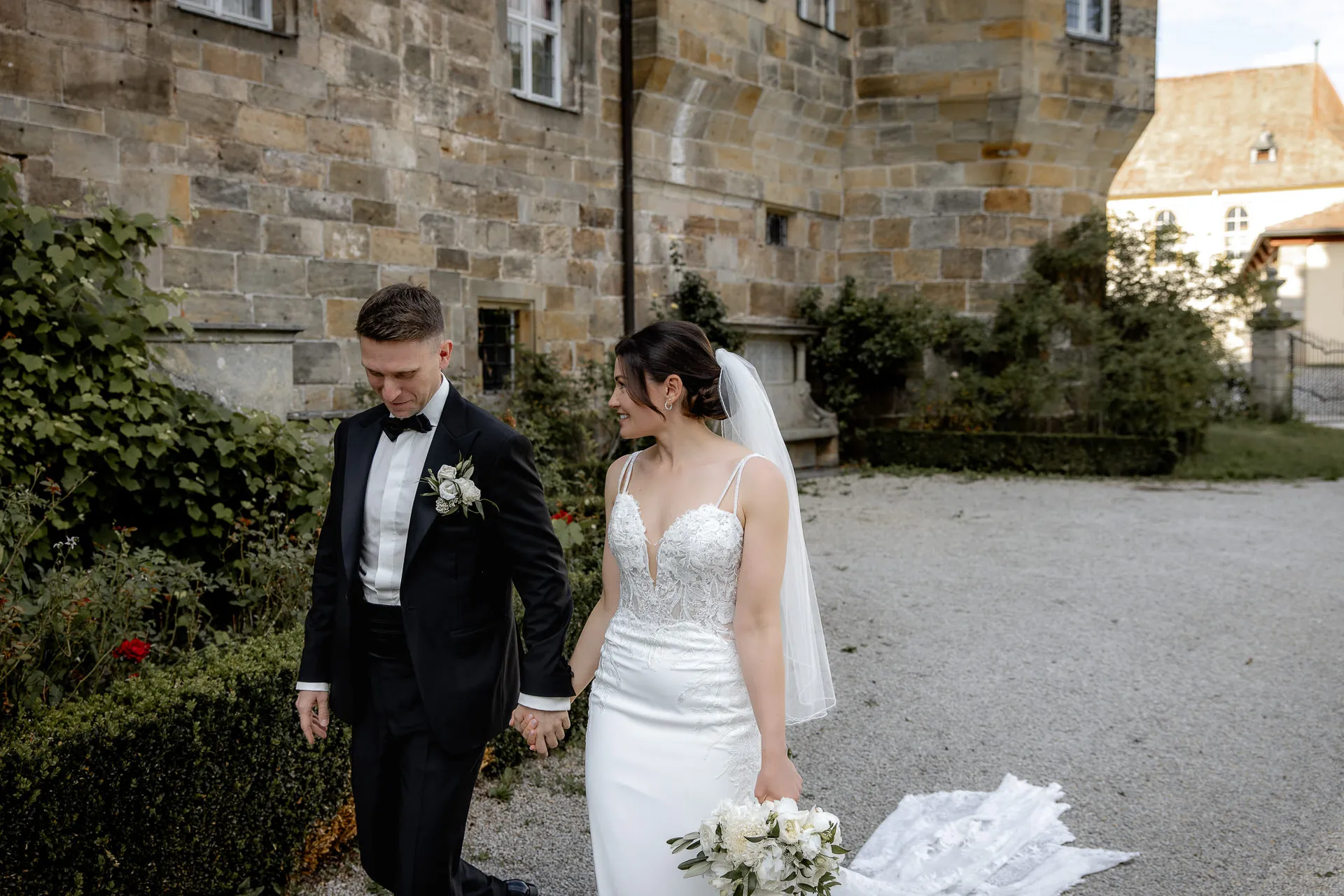 Bride and groom walking hand in hand through Schloss Eyrichshof courtyard with lace veil and bouquet