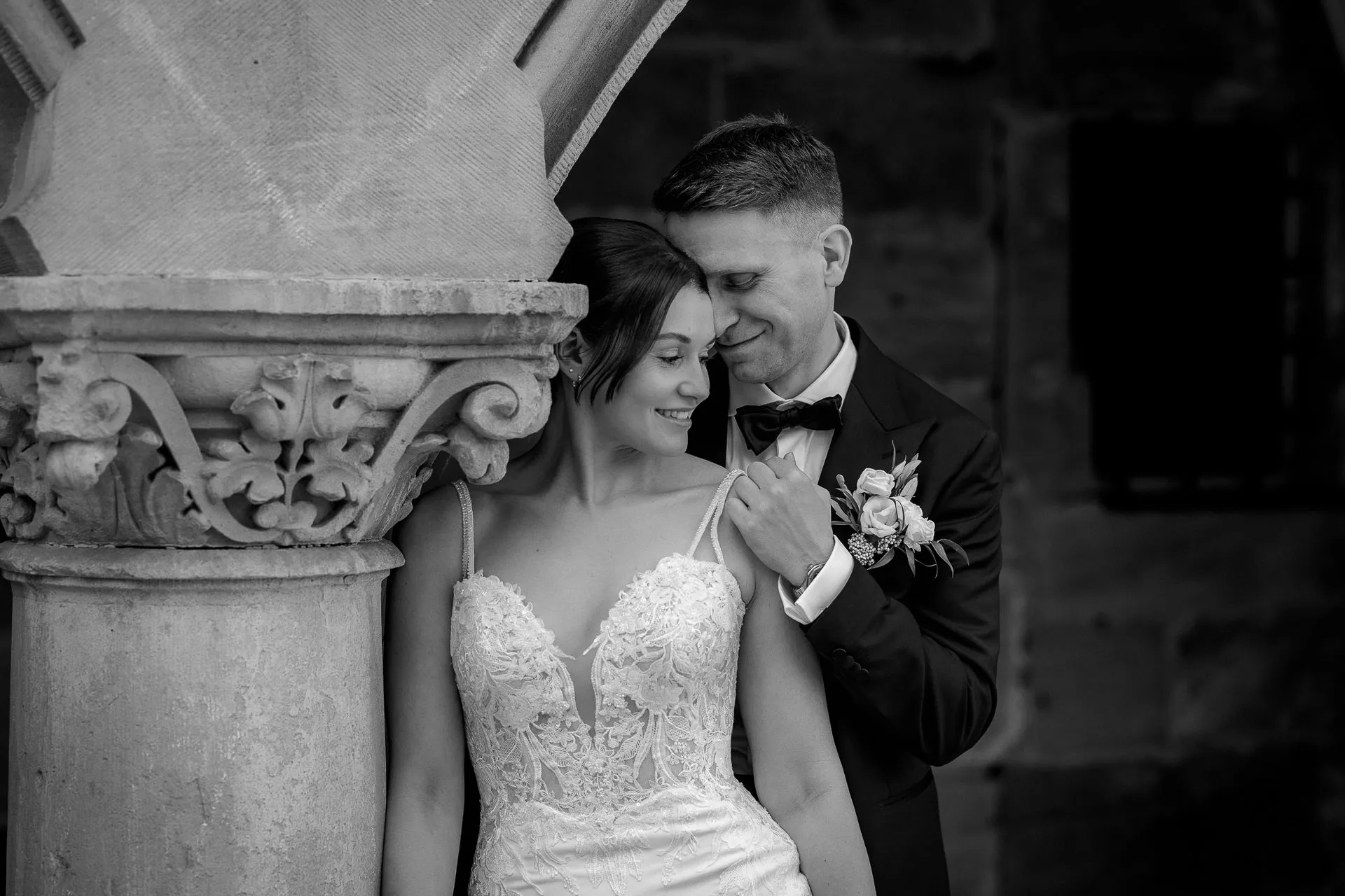 Intimate moment between bride and groom at stone column Schloss Eyrichshof in black and white