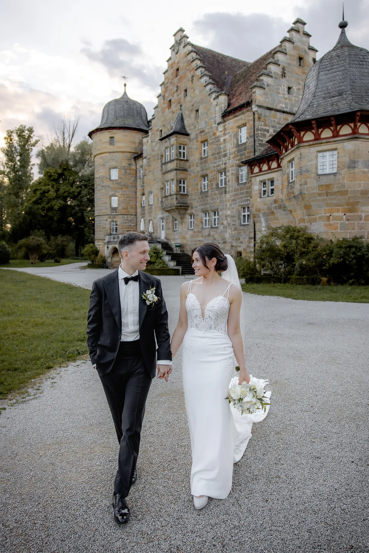 Bride and groom walking in front of impressive Schloss Eyrichshof facade at evening wedding with bouquet
