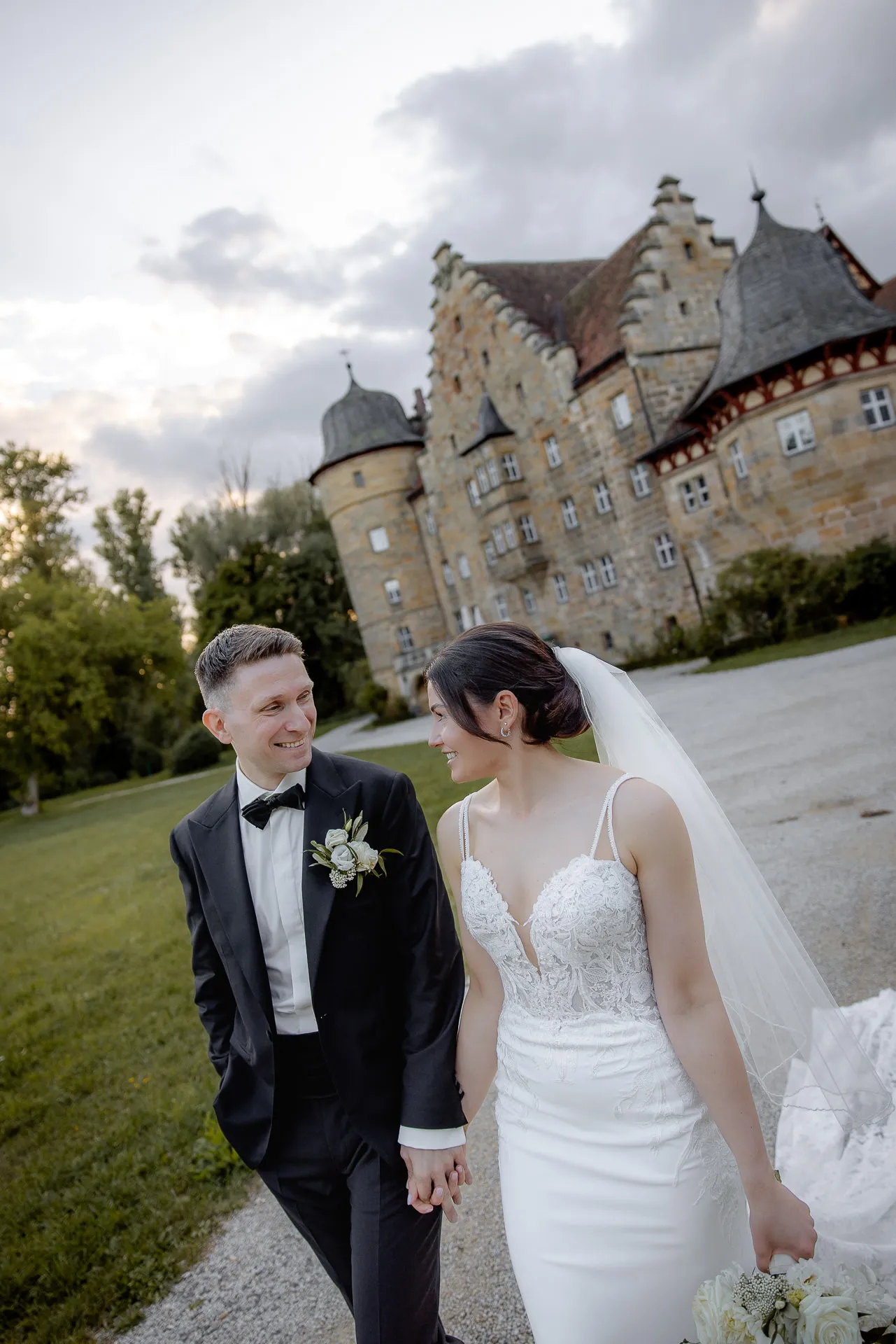 Happy bride and groom in front of impressive Schloss Eyrichshof at evening wedding with dramatic sky