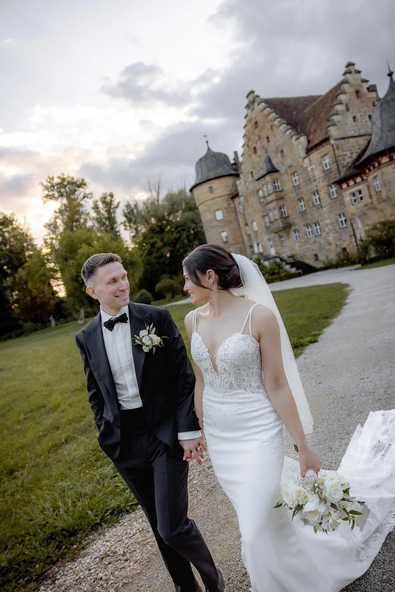 Romantic bride and groom in front of Schloss Eyrichshof towers at evening wedding with bouquet