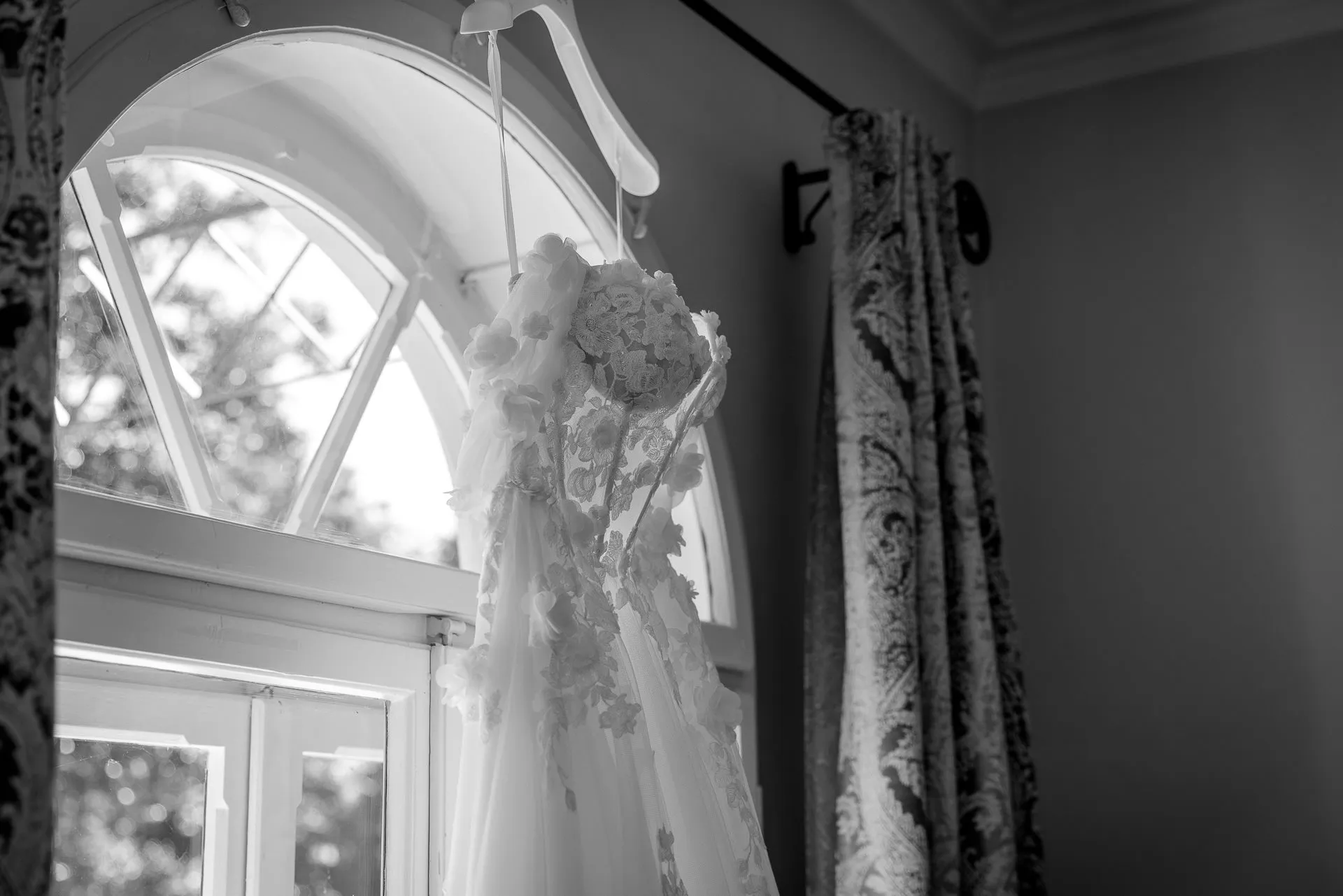 Romantic wedding dress with floral appliqués hanging in La Villa window