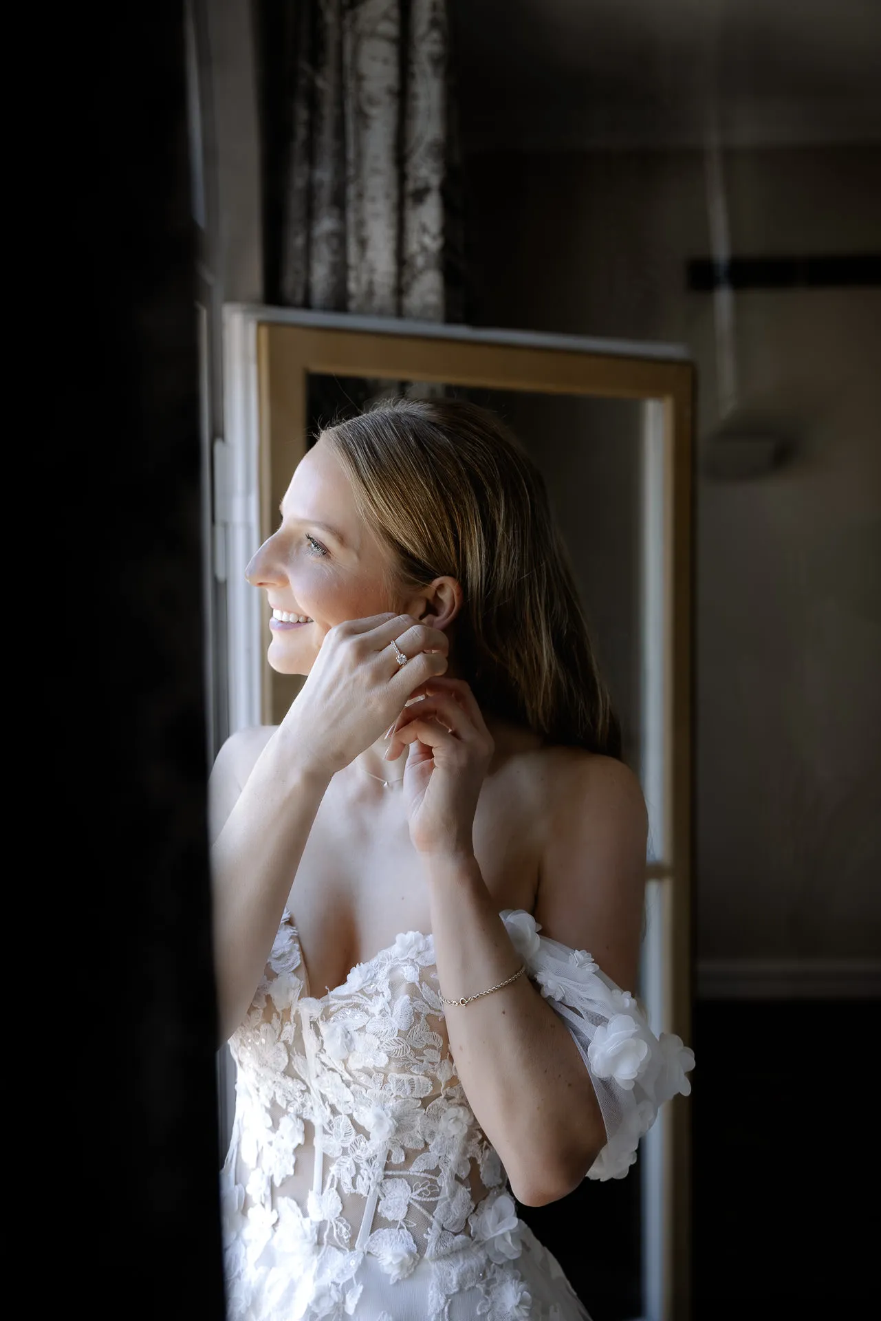 Bride putting on earrings in window light at La Villa
