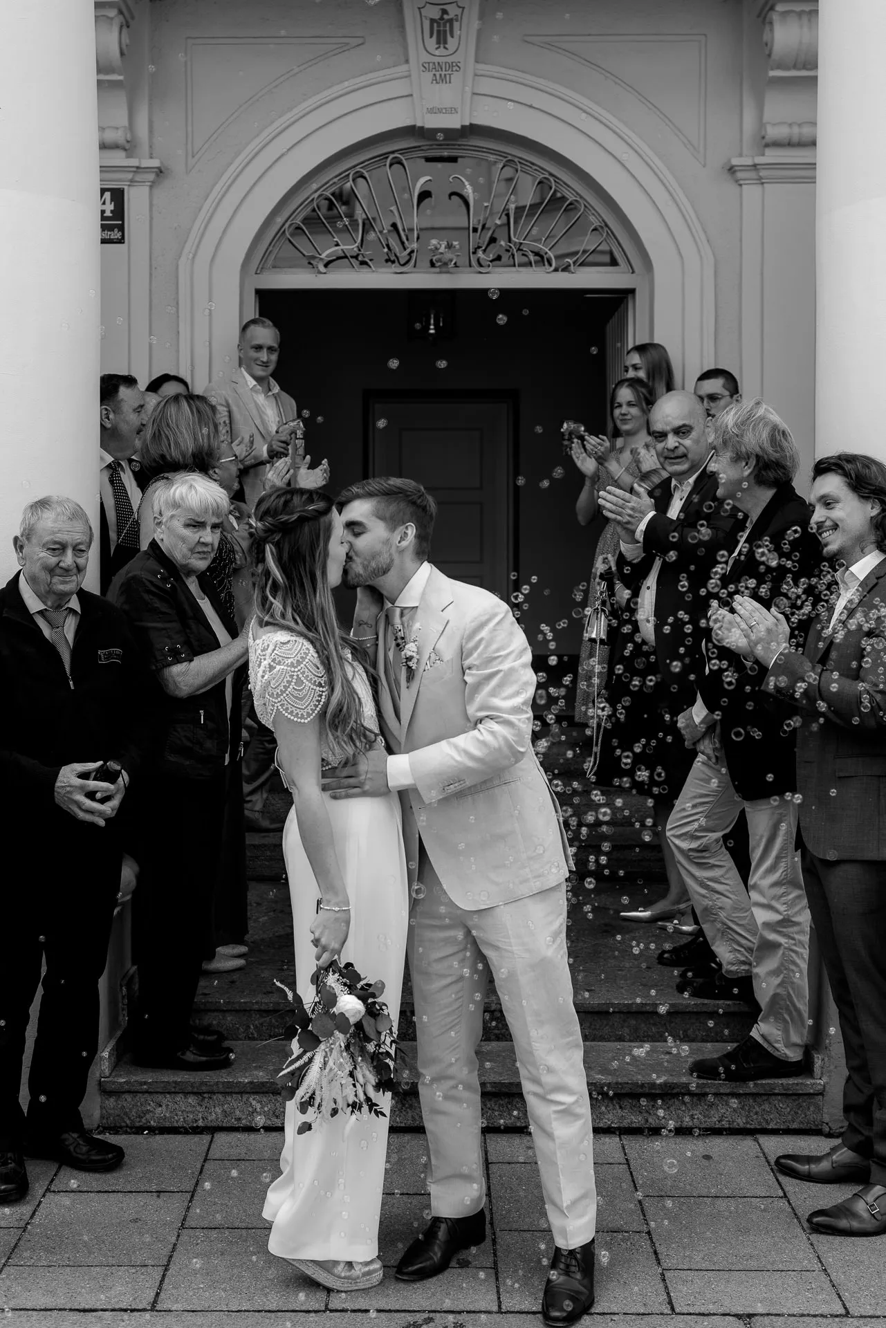 Couple kiss in front of Standesamt Mandlstraße with guests – emotional wedding photography