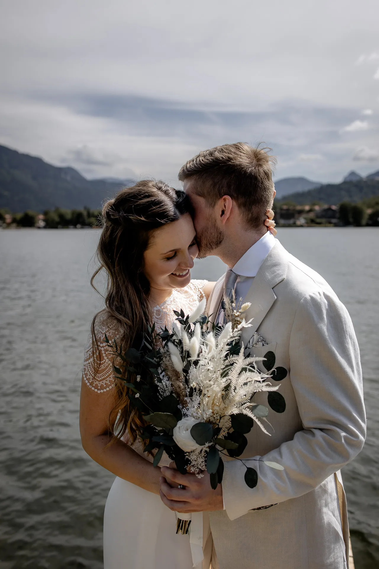 Romantic couple kiss at Lake Tegernsee with boho bouquet – emotional wedding photography