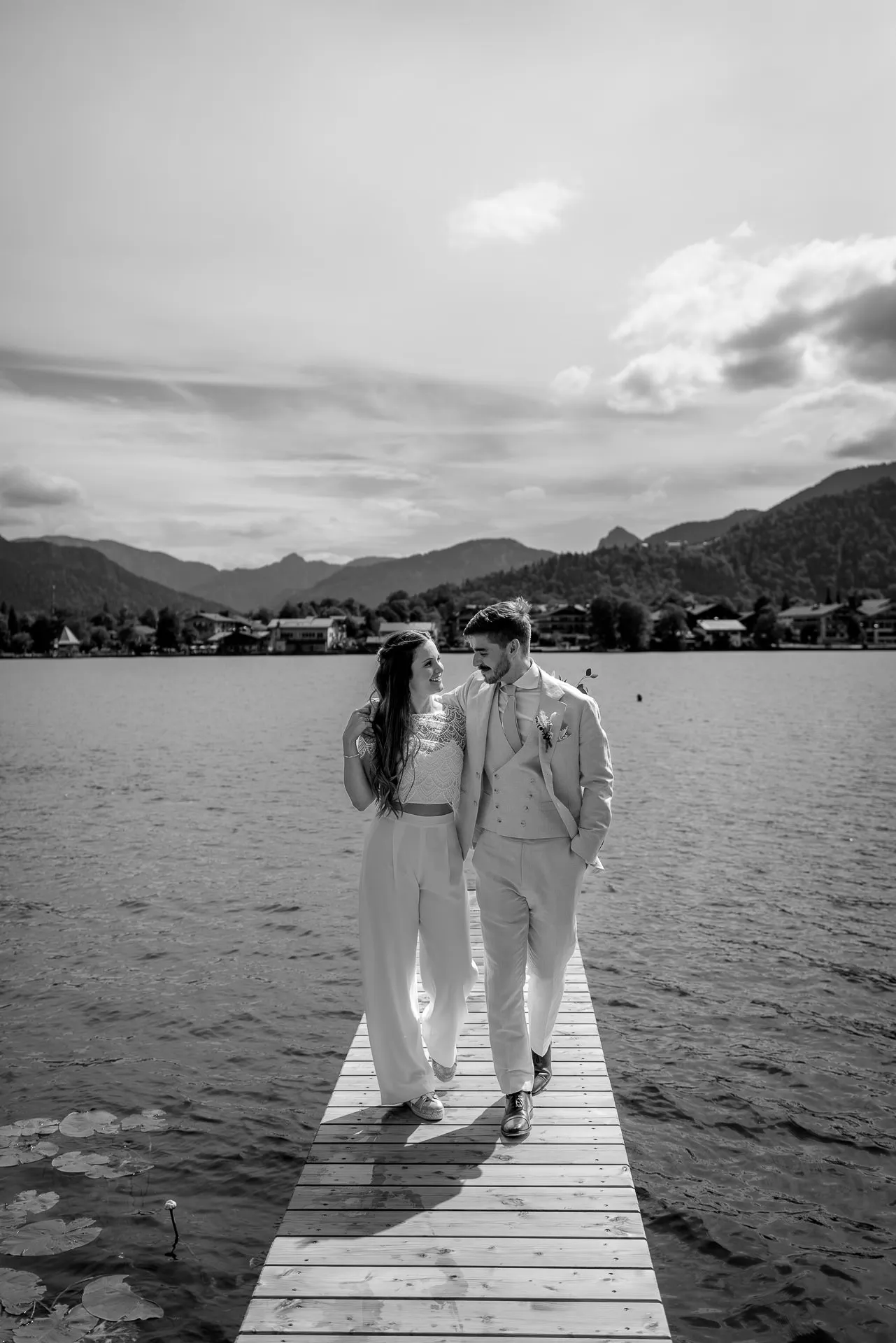 Bride and groom on pier at Lake Tegernsee with mountain panorama – artistic wedding photography in black and white