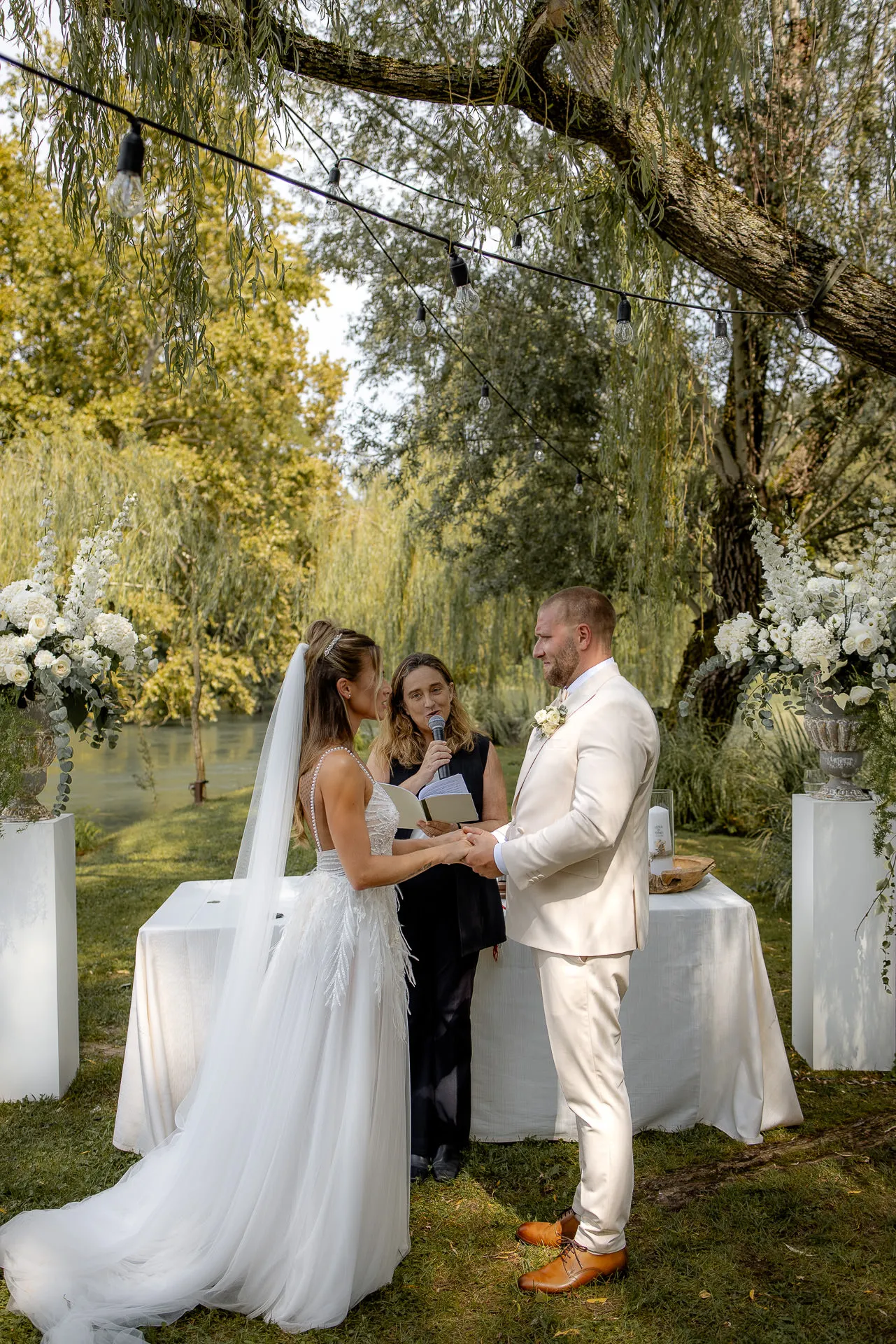 Elegant wedding ceremony by the river with white floral decoration and weeping willows