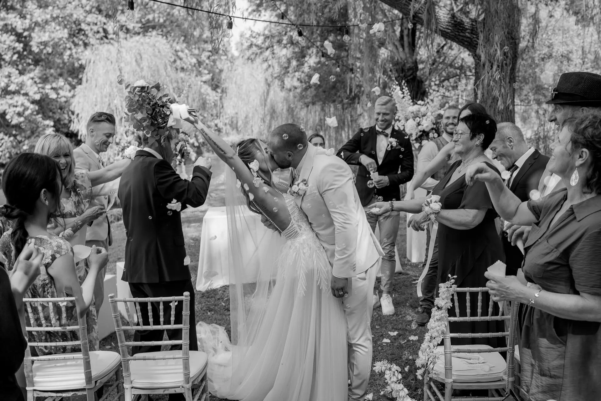 Cheering wedding guests celebrate the newlyweds in black and white