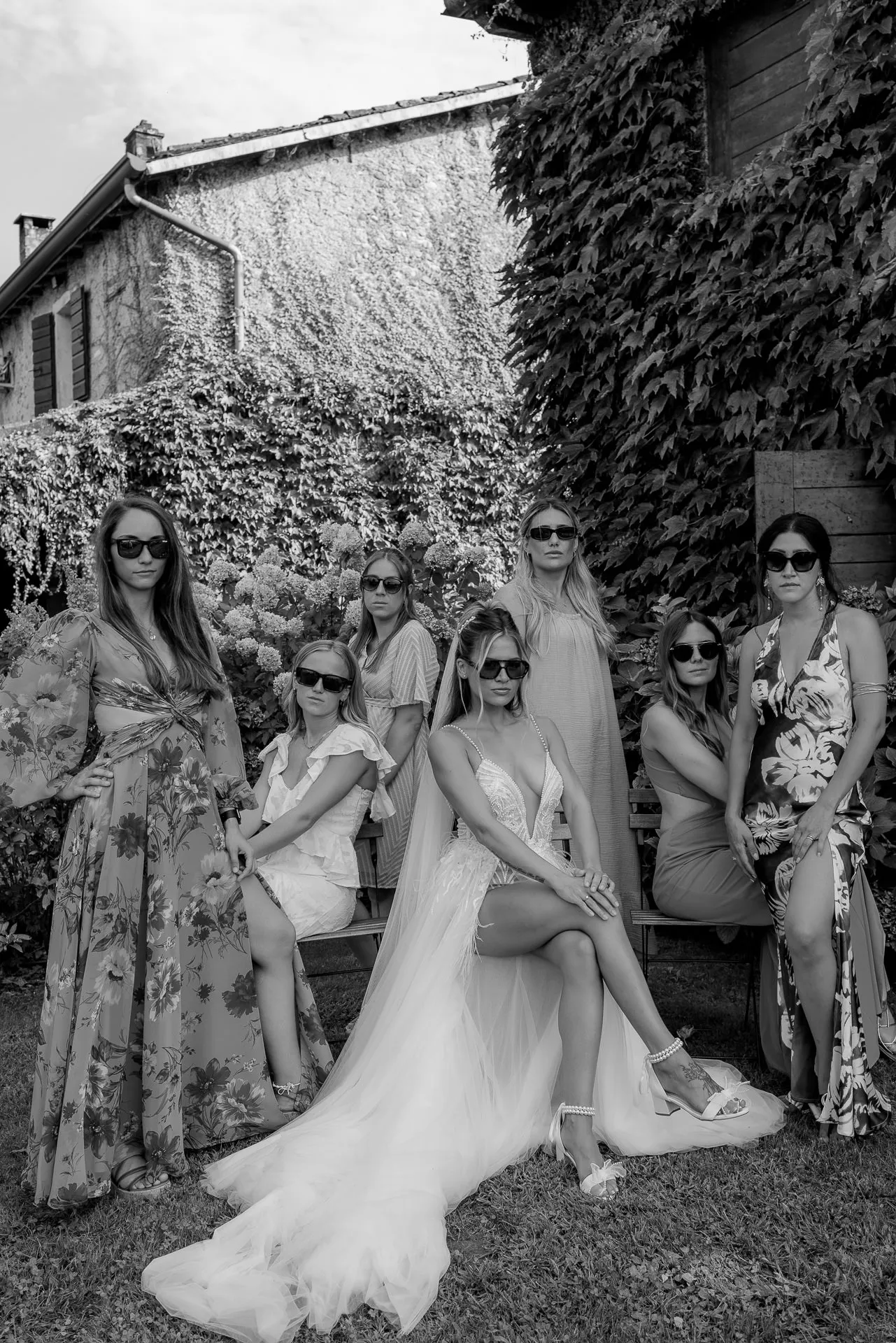 Bride with friends in elegant dresses by ivy-covered wall in Italy