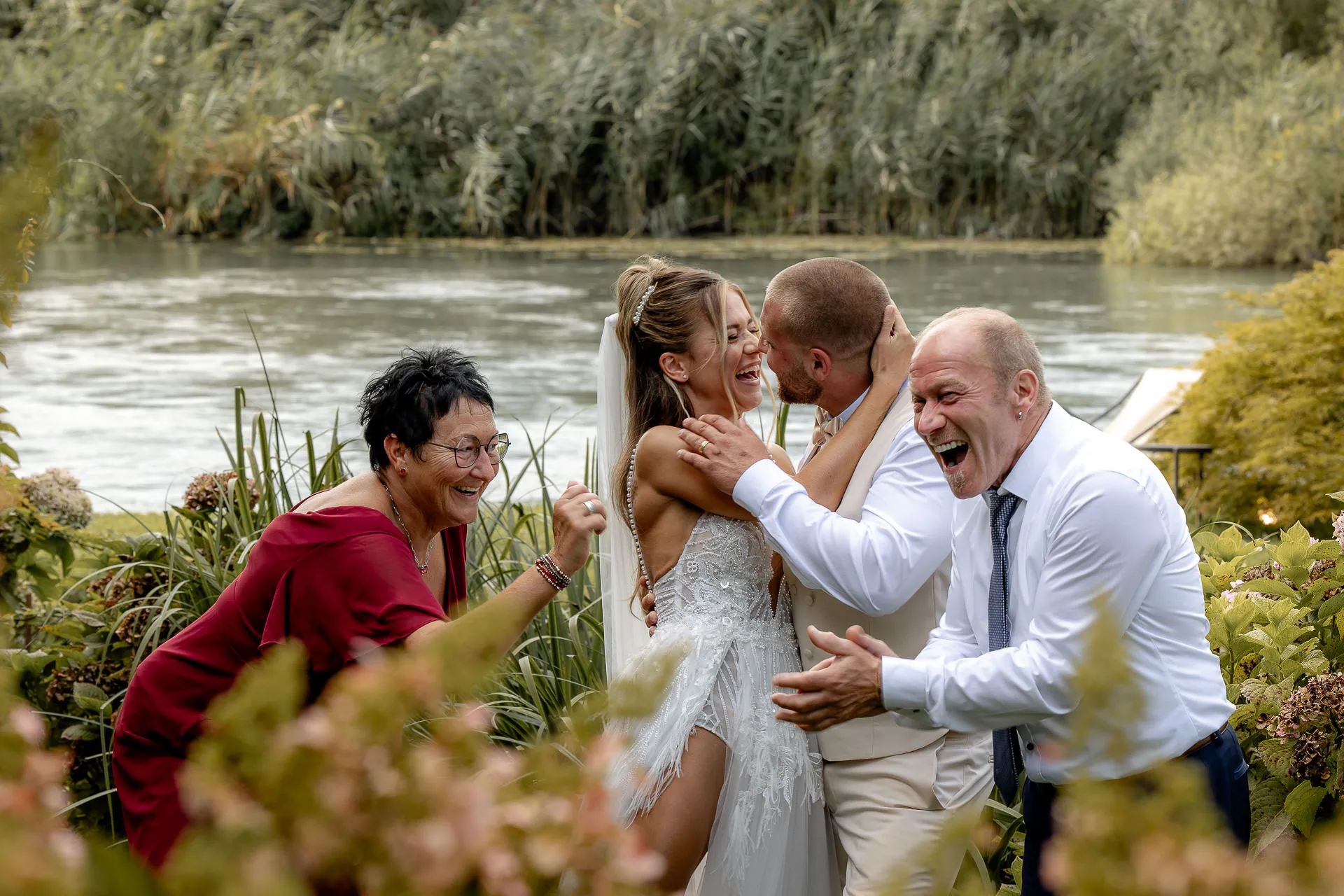 Cheering wedding guests celebrating bride's kiss by river at La Finestra