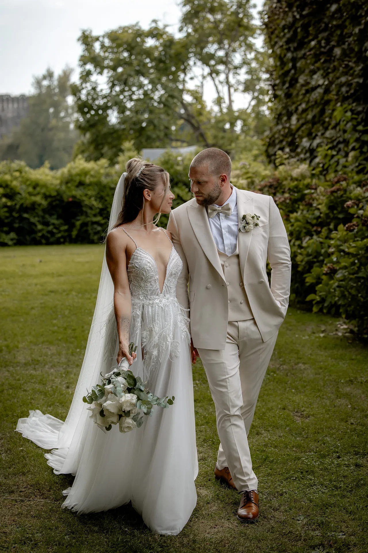 Elegant couple in garden with eucalyptus bouquet and groom in beige suit