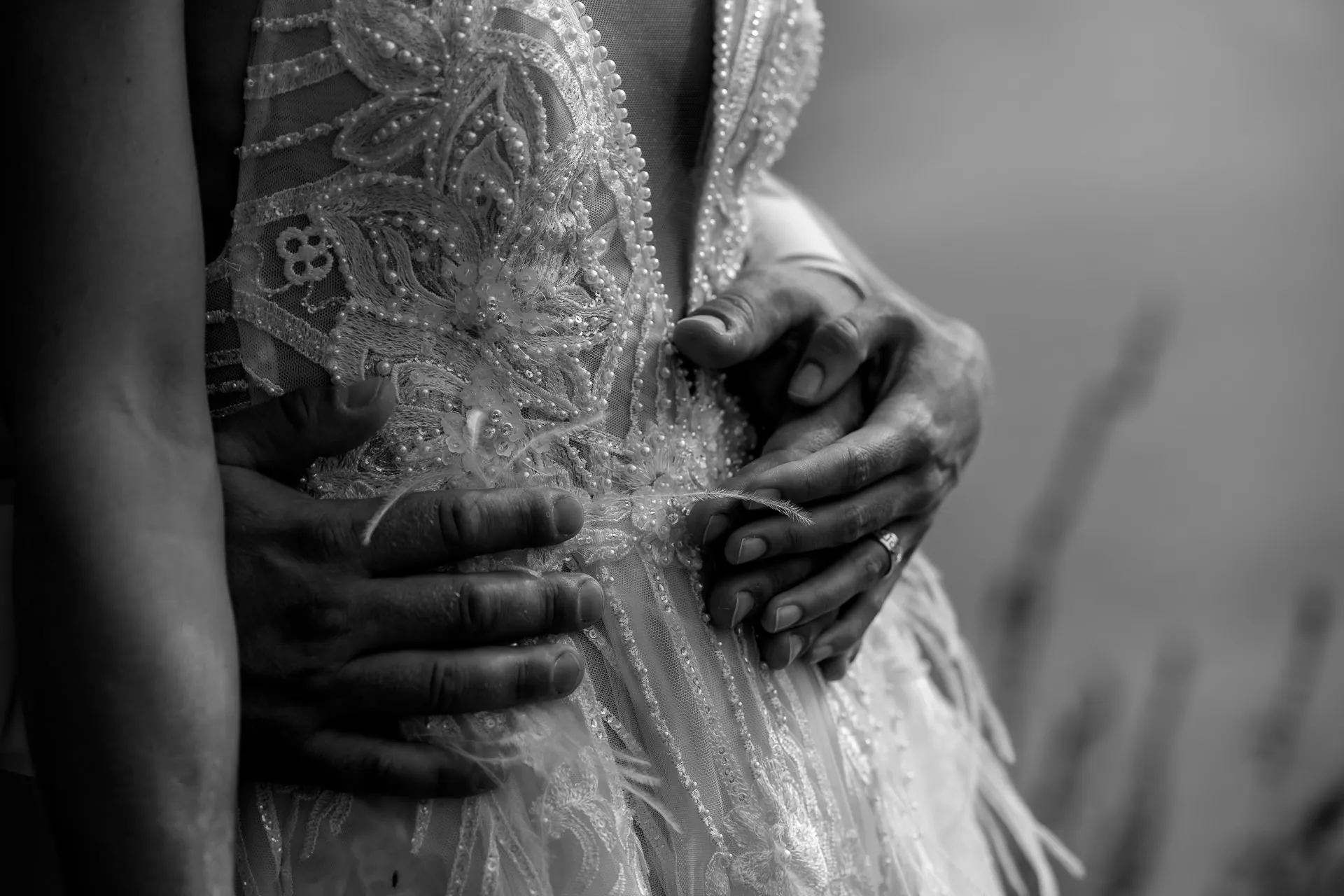 Close-up of wedding dress details with beaded embroidery and couple's hands