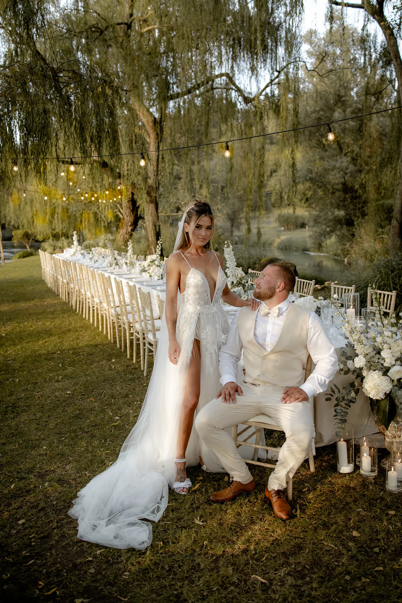 Glamorous couple portrait at twilight with string lights by riverside