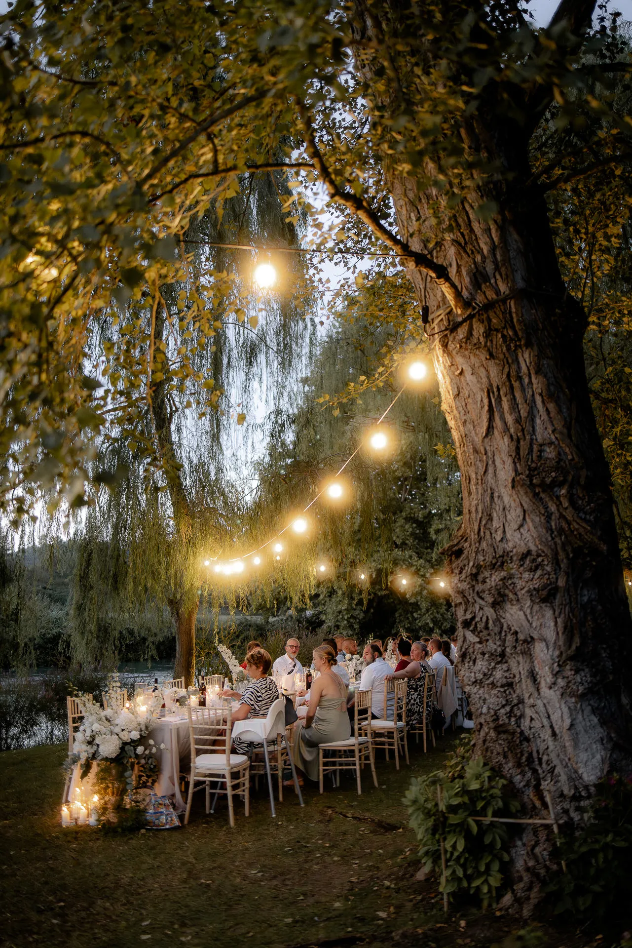 Magical night wedding under ancient trees with string lights by Italian riverside