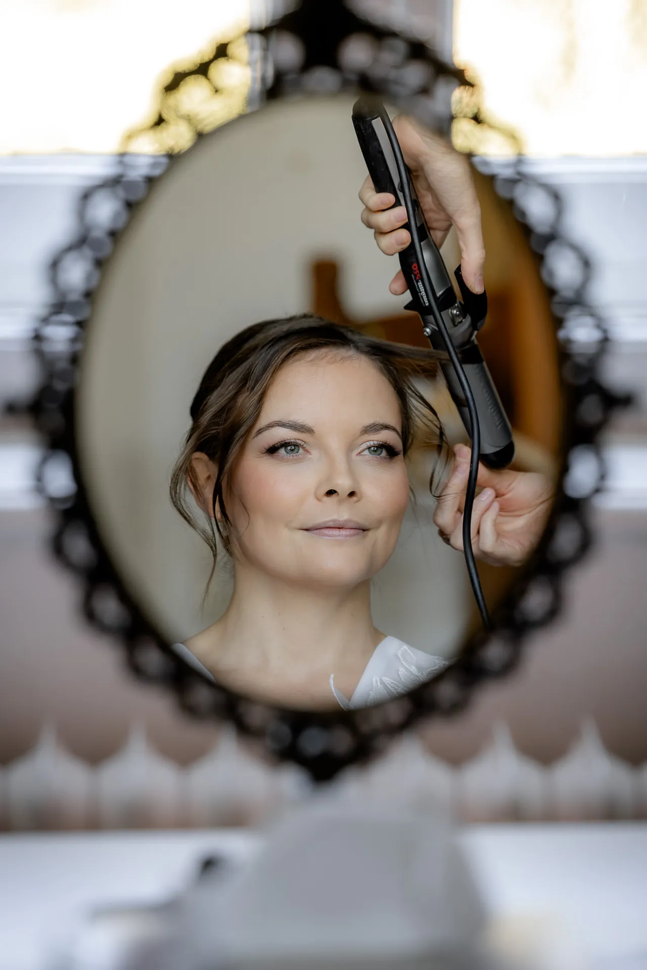 Bride mirror reflection during wedding preparation with curling iron at Gut Sonnenhausen