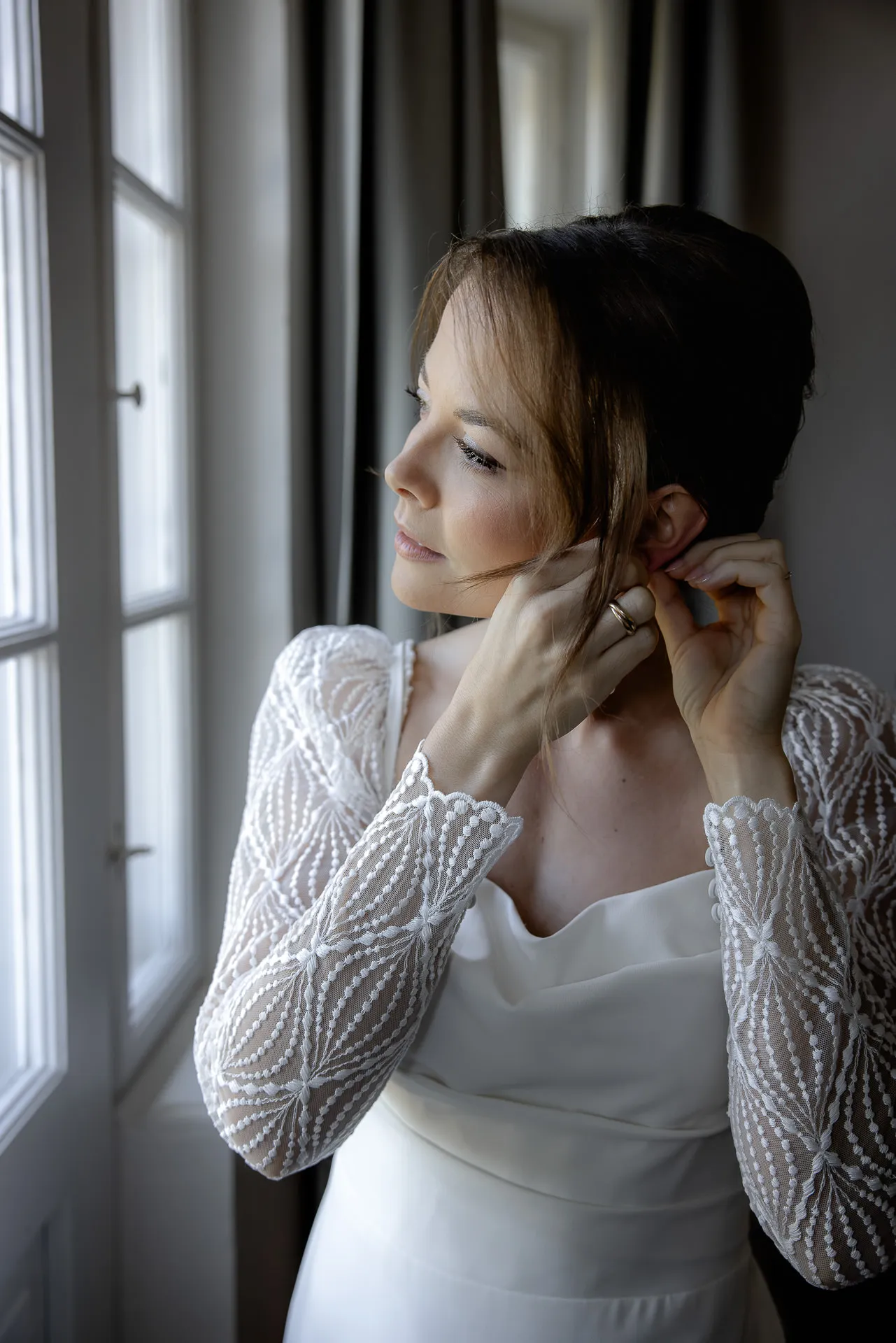 Bride putting on earrings by window at Gut Sonnenhausen wedding
