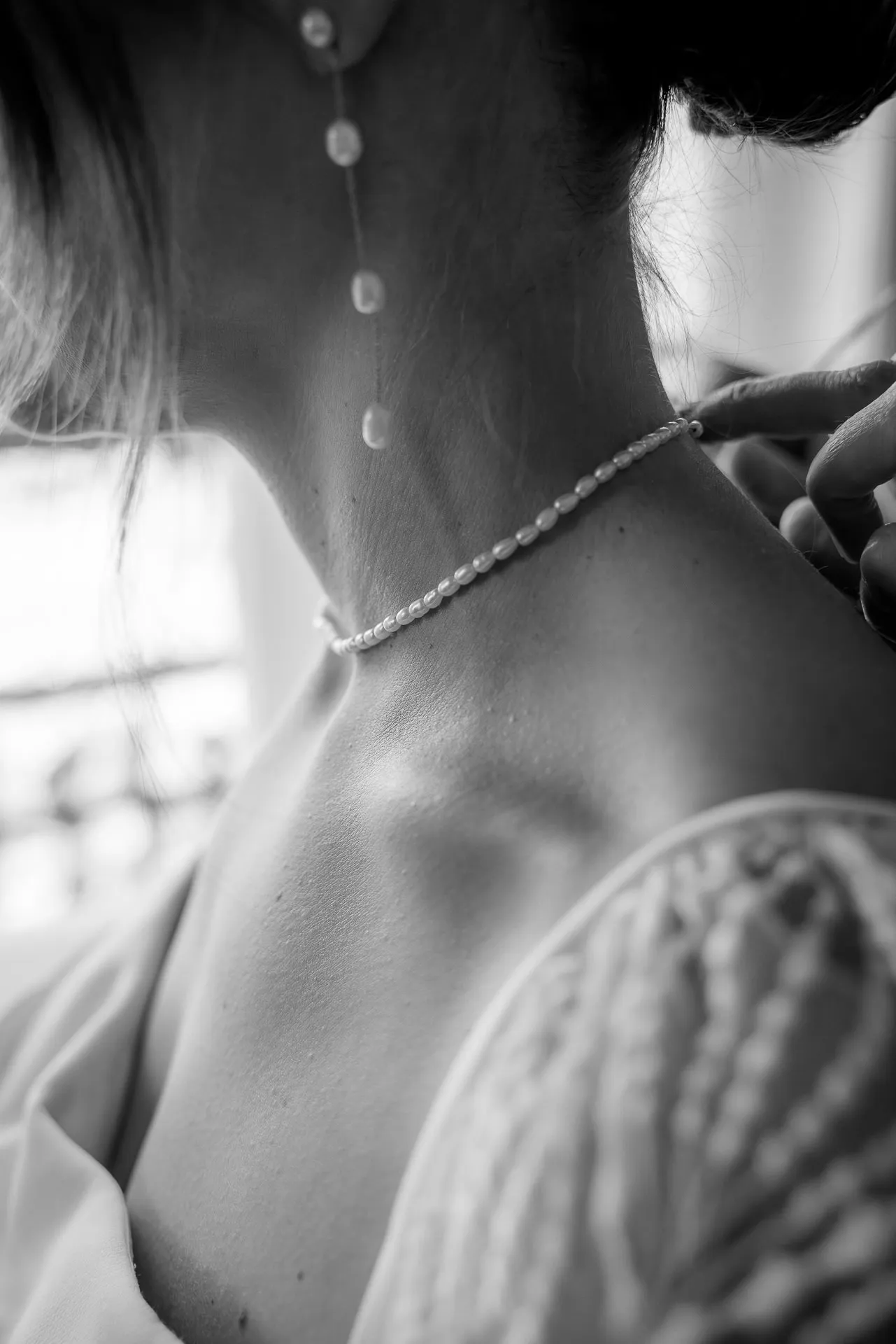 Bride getting pearl necklace fastened in black and white at Gut Sonnenhausen