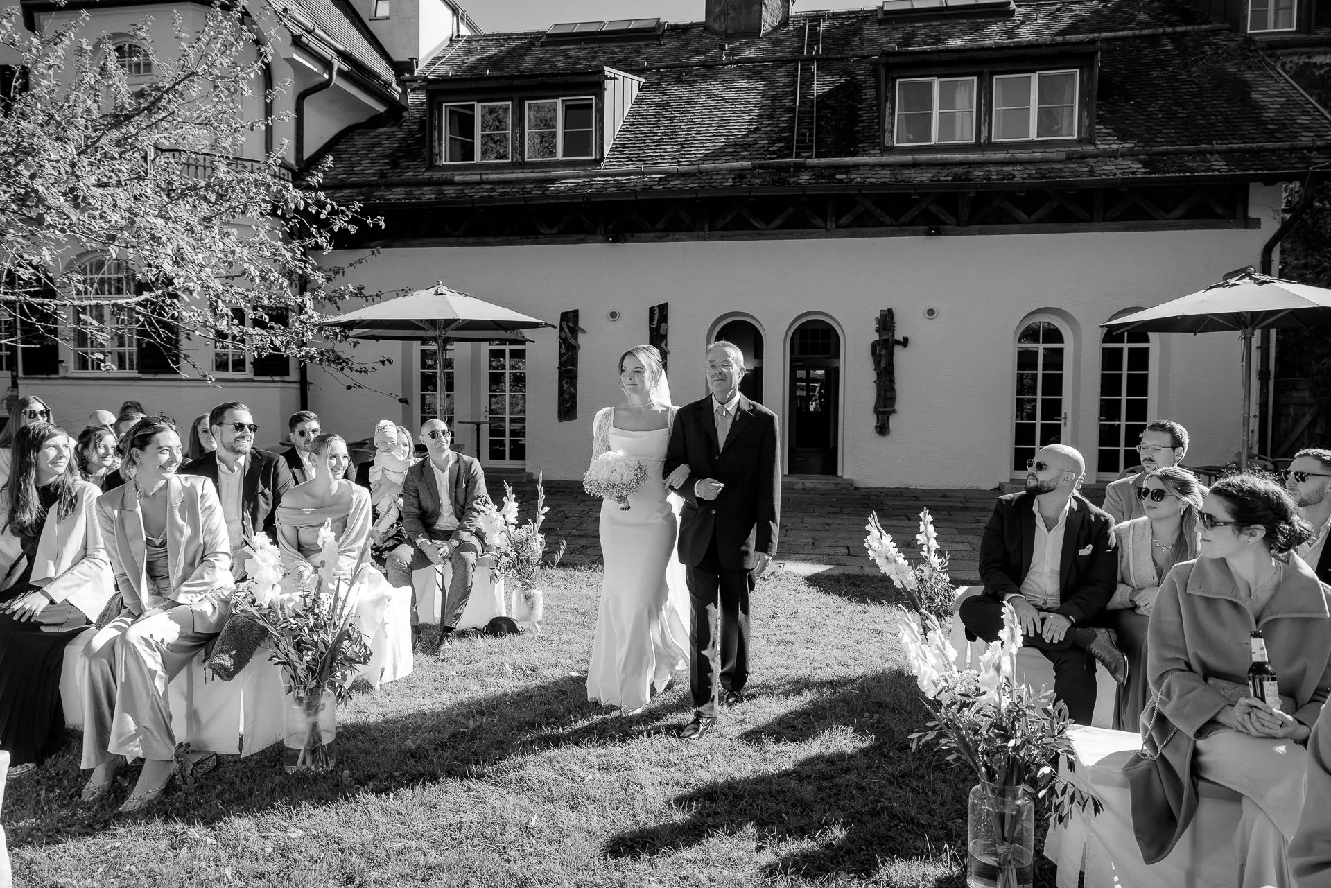 Bride walking down aisle with father at outdoor ceremony at Gut Sonnenhausen in black and white