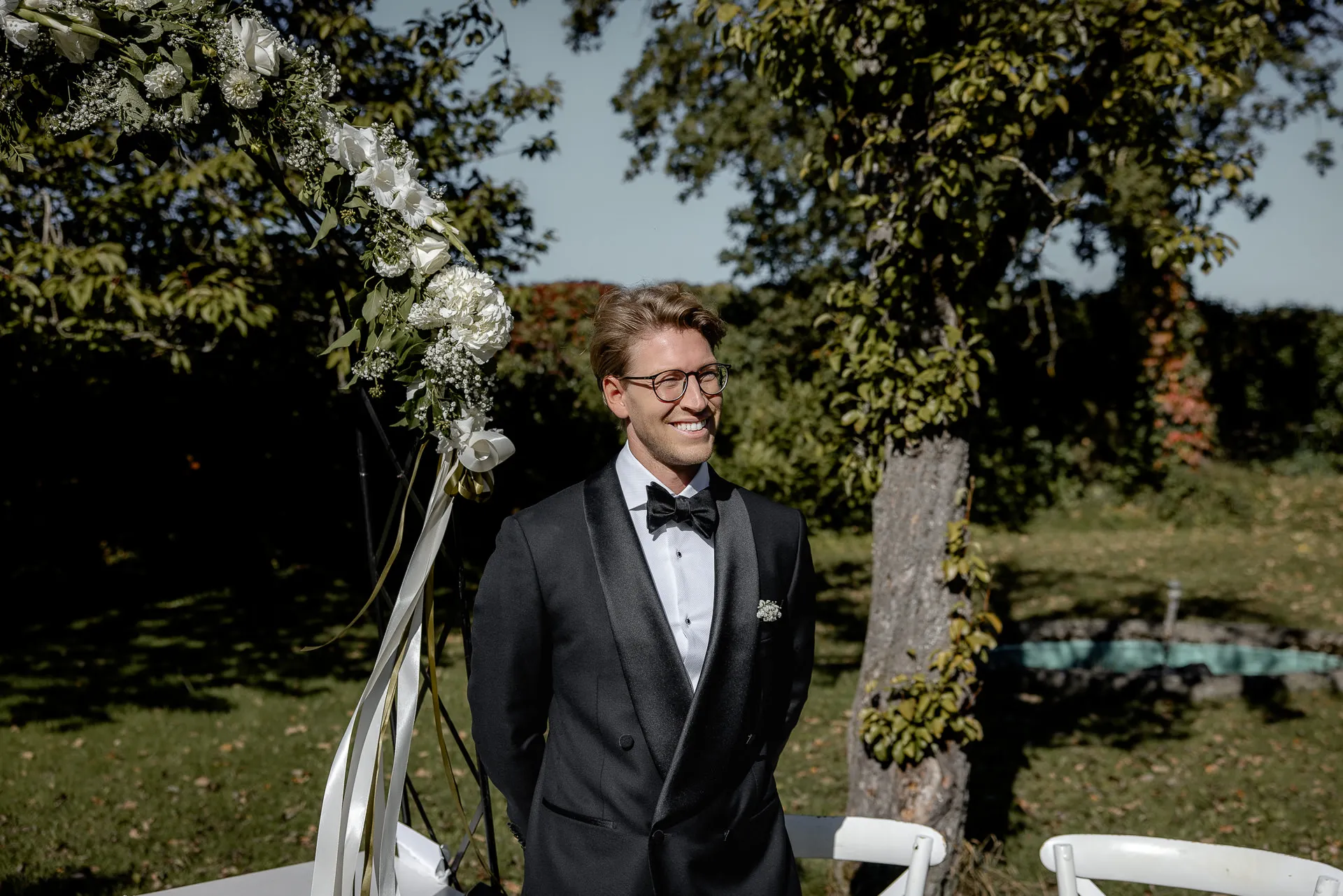 Groom smiling waiting at wedding arch during outdoor ceremony at Gut Sonnenhausen