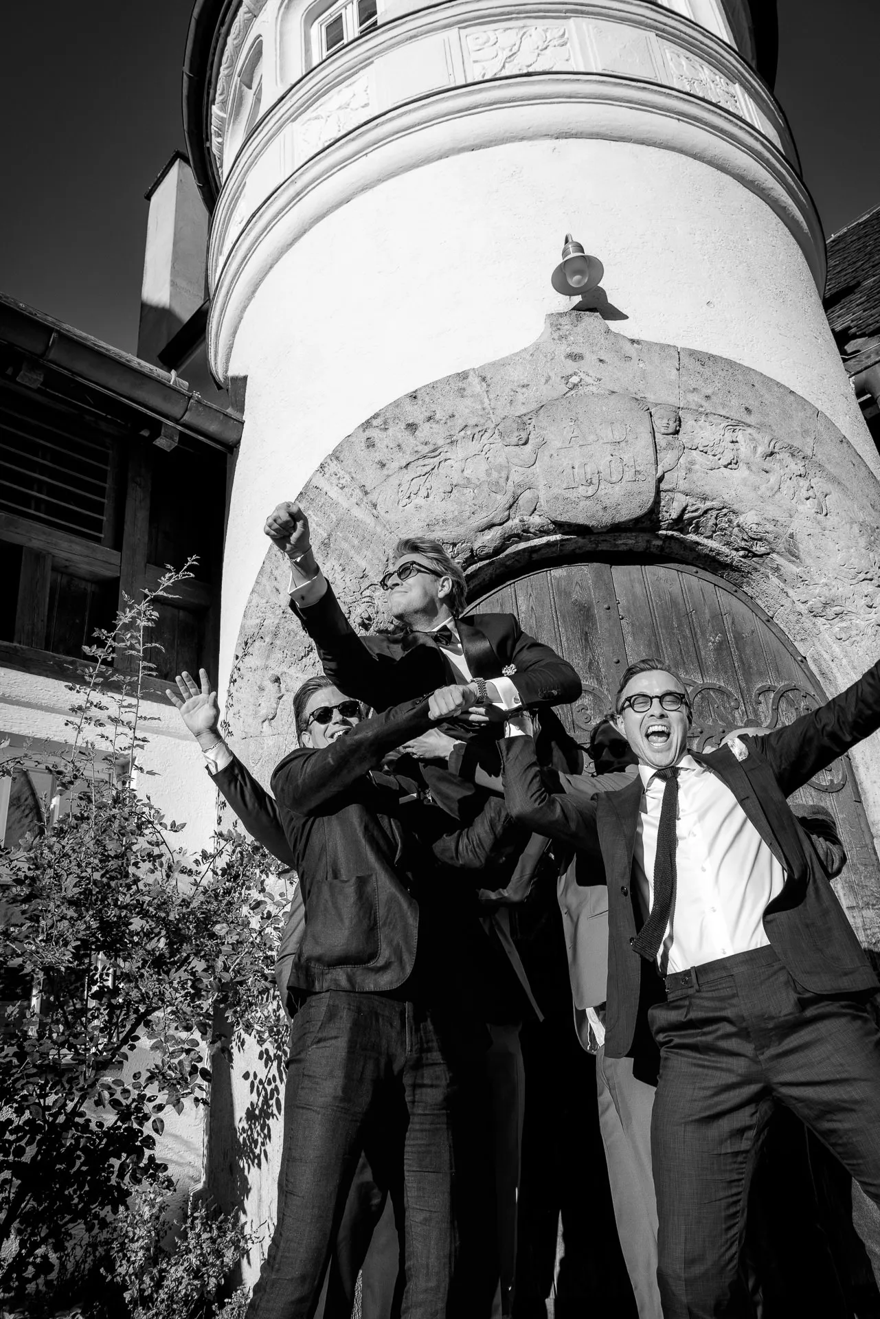 Wedding guests lifting man on shoulders at celebration at Gut Sonnenhausen in black and white