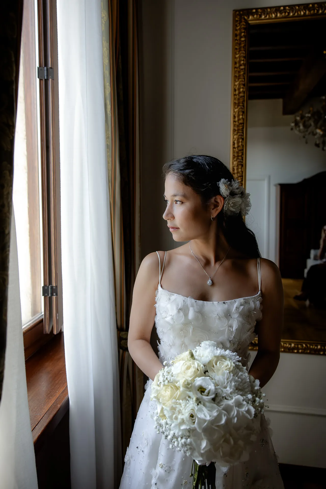 Bride with white bouquet gazing thoughtfully out window at Villa Cariola