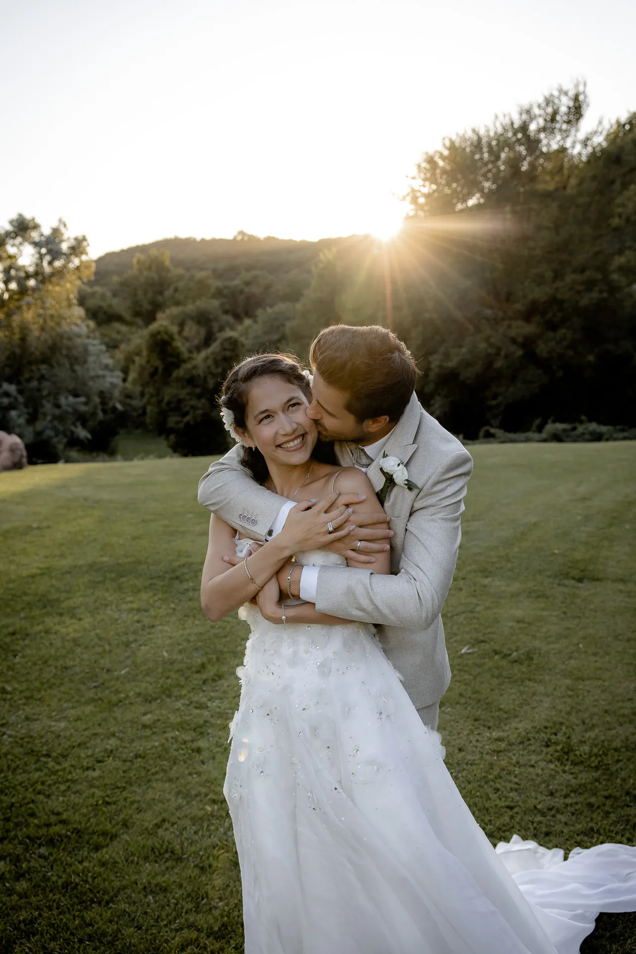 Laughing bride embraced by groom in golden sunset light