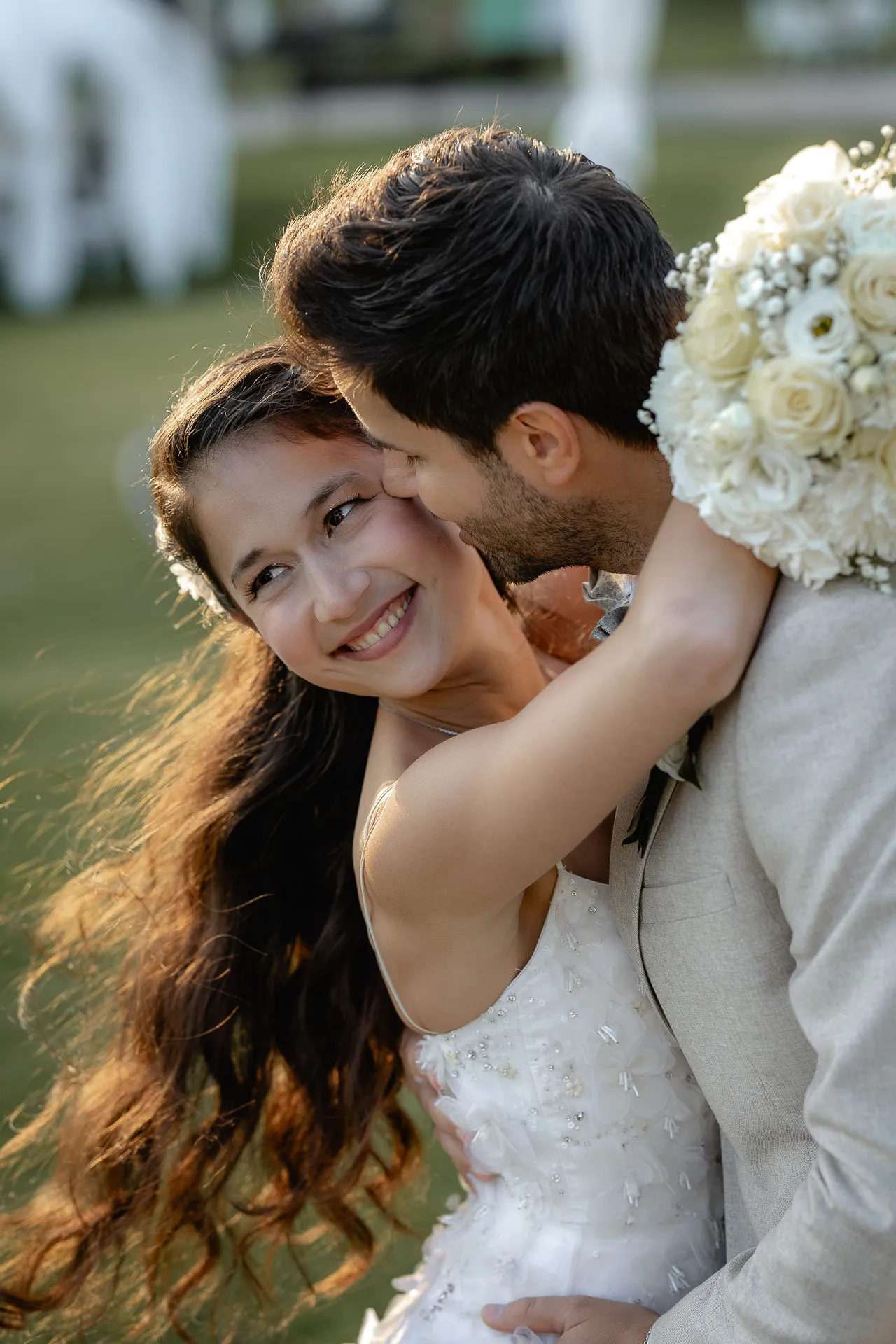 Radiant bride embraced by groom with bouquet at sunset