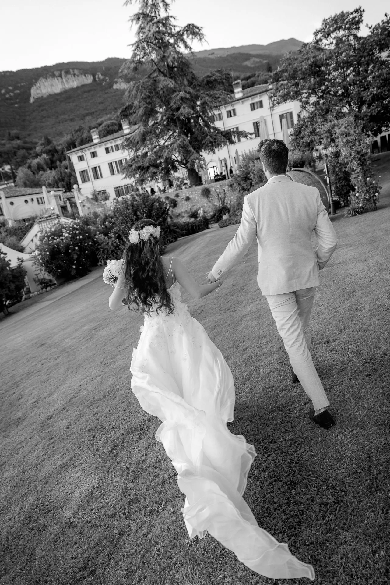 Wedding couple walking hand in hand in front of Villa Cariola with mountain panorama in black and white